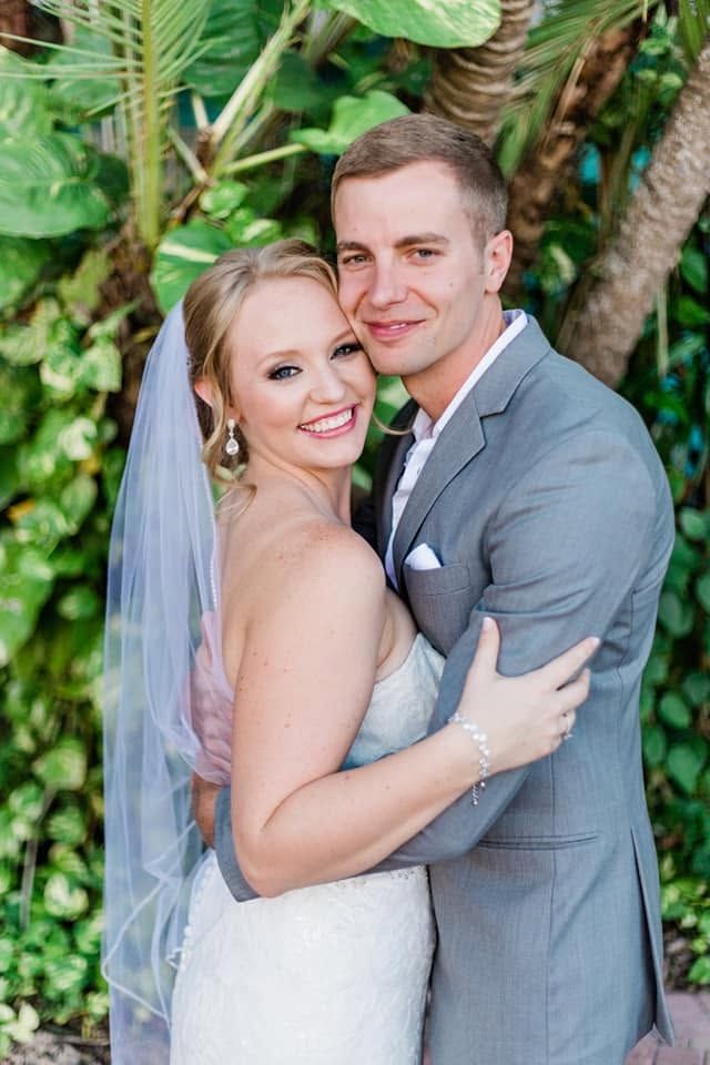 Smiling bride and groom embrace in close portrait surrounded by lush tropical greenery.