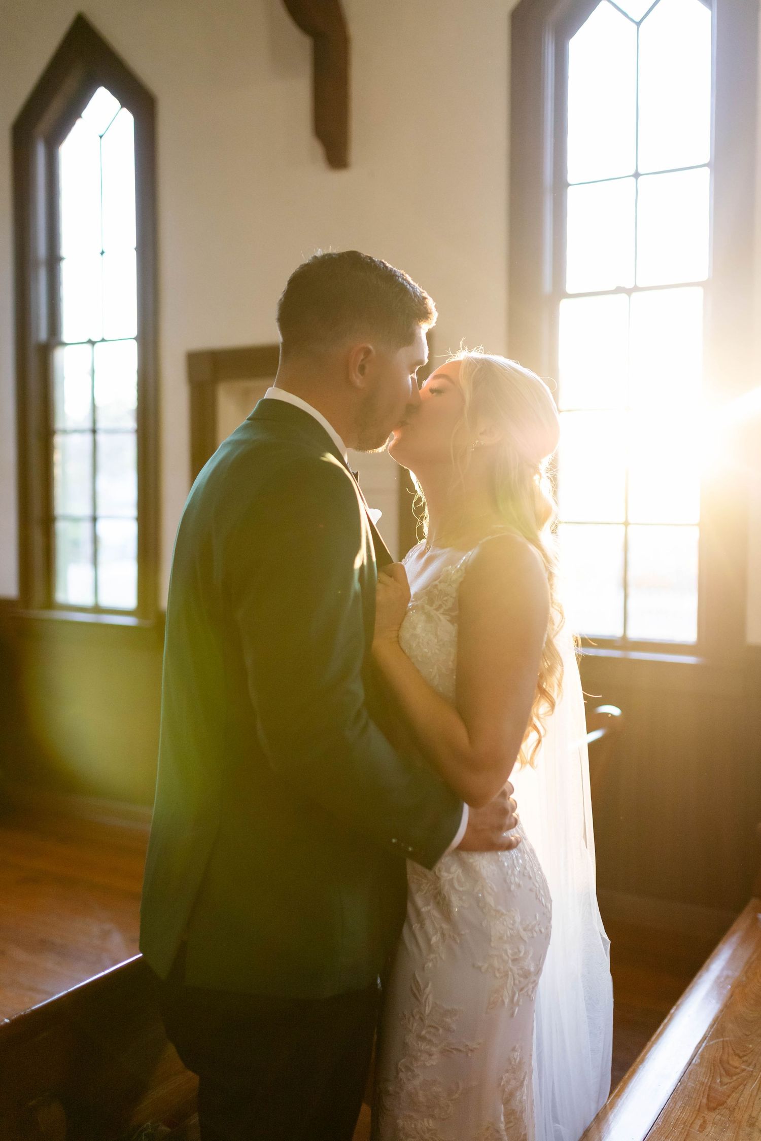 Bride and groom sharing their first kiss bathed in golden sunlight streaming through chapel windows in Dunedin.