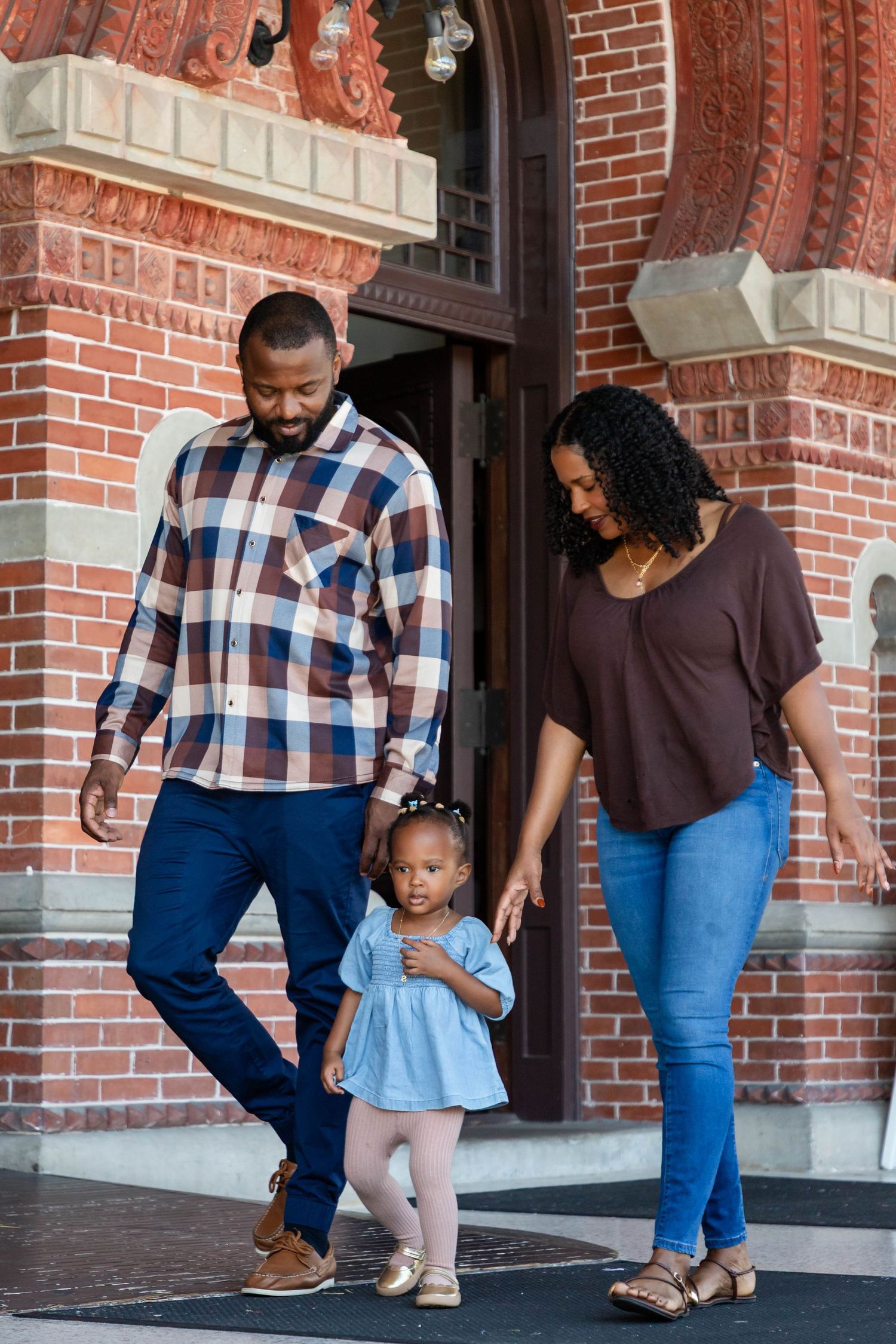 Black family with young toddler girl walks out of ornate brick building entrance together at the University of Tampa.
