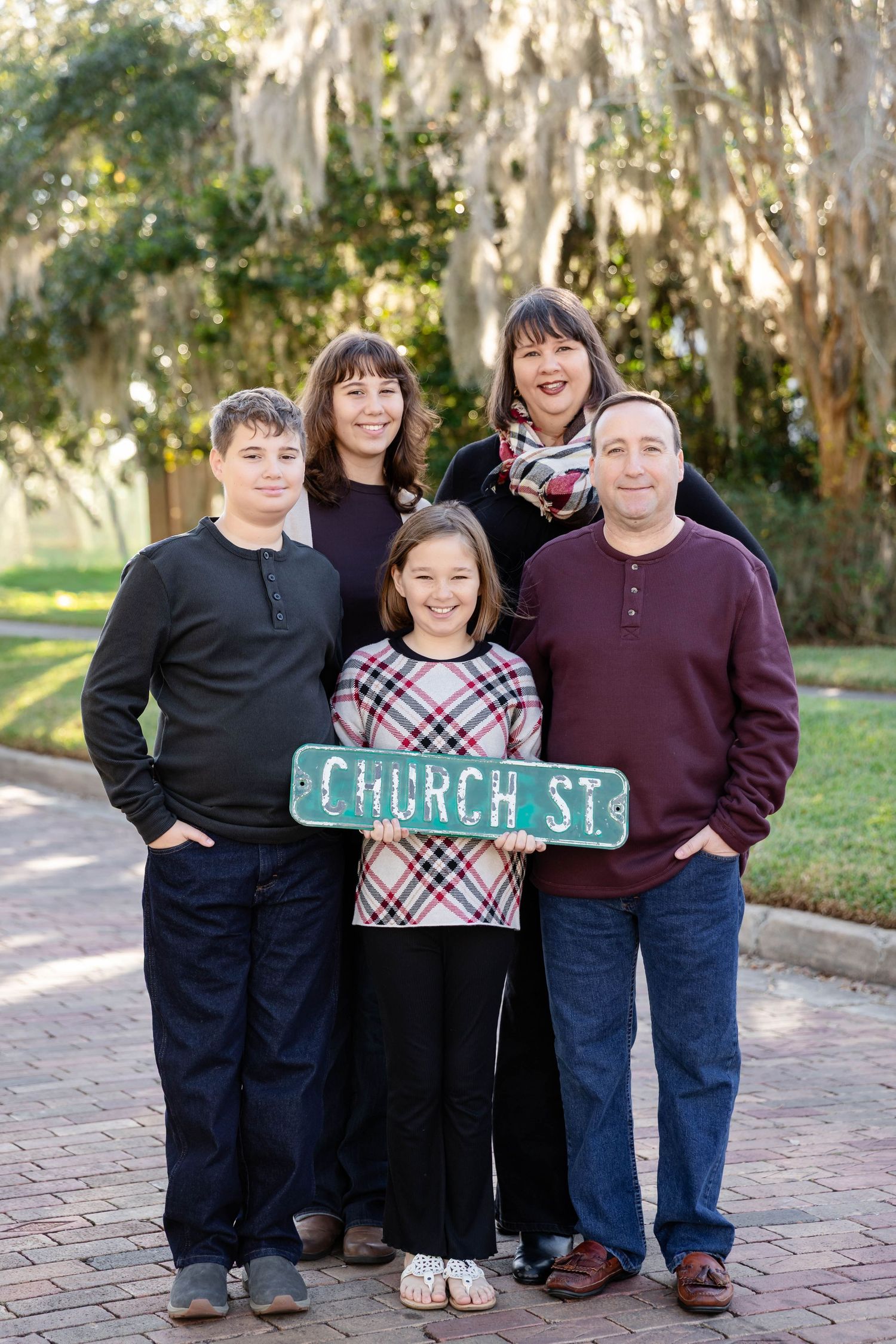 Family of five posing outdoors holding a vintage Church St. street sign on a brick pathway.