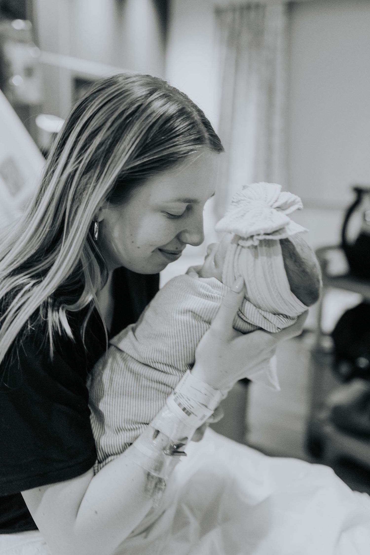 Black and white photo of new mother tenderly holding and smelling her swaddled newborn in hospital.