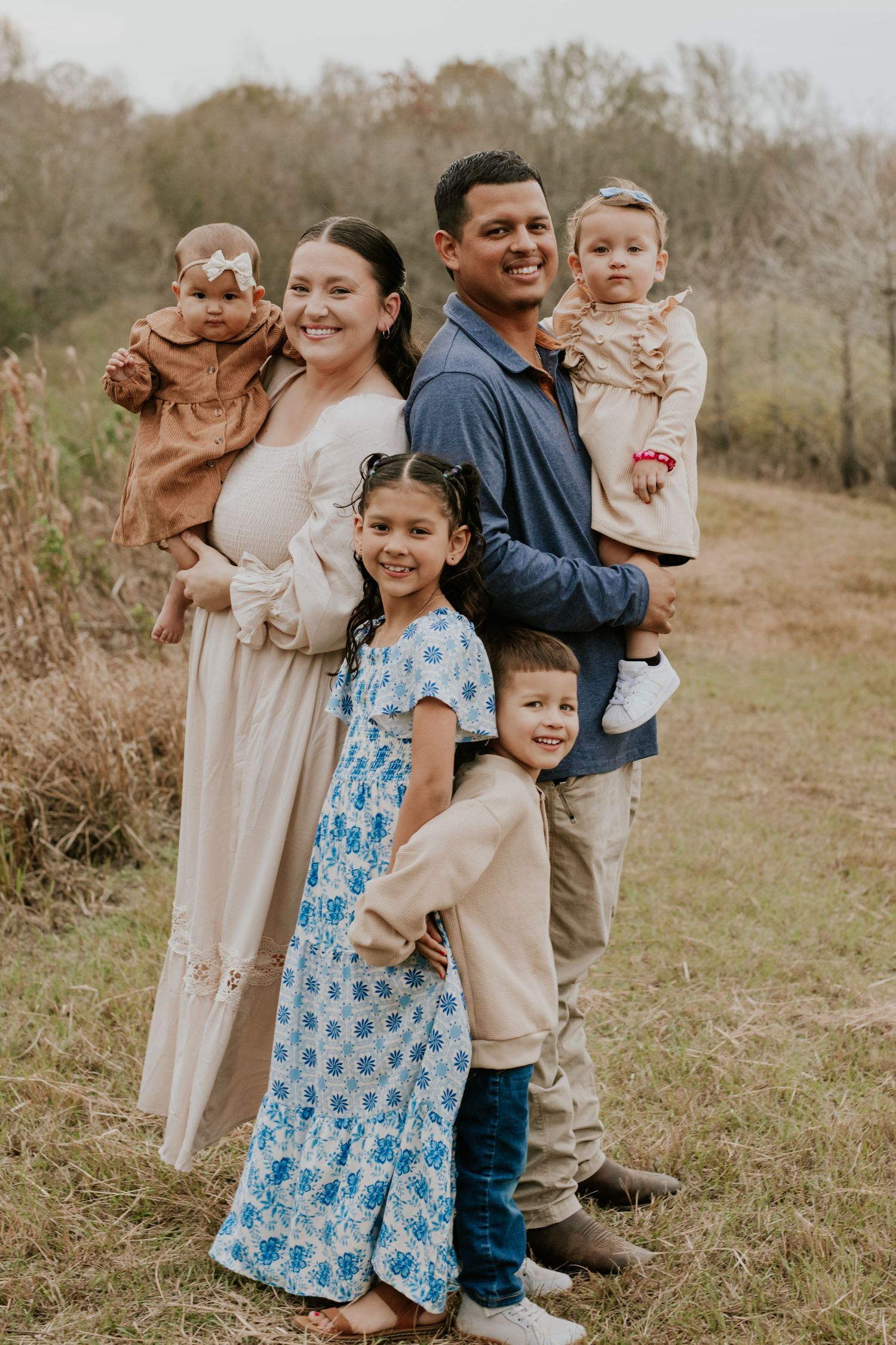 Joyful family of six smiles together in an autumn field with golden grass.