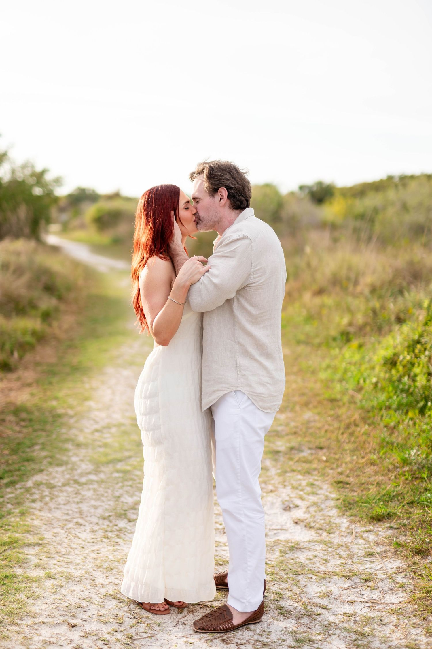 Couple sharing a romantic kiss on a sandy path surrounded by golden hour natural landscape at Honeymoon Island.