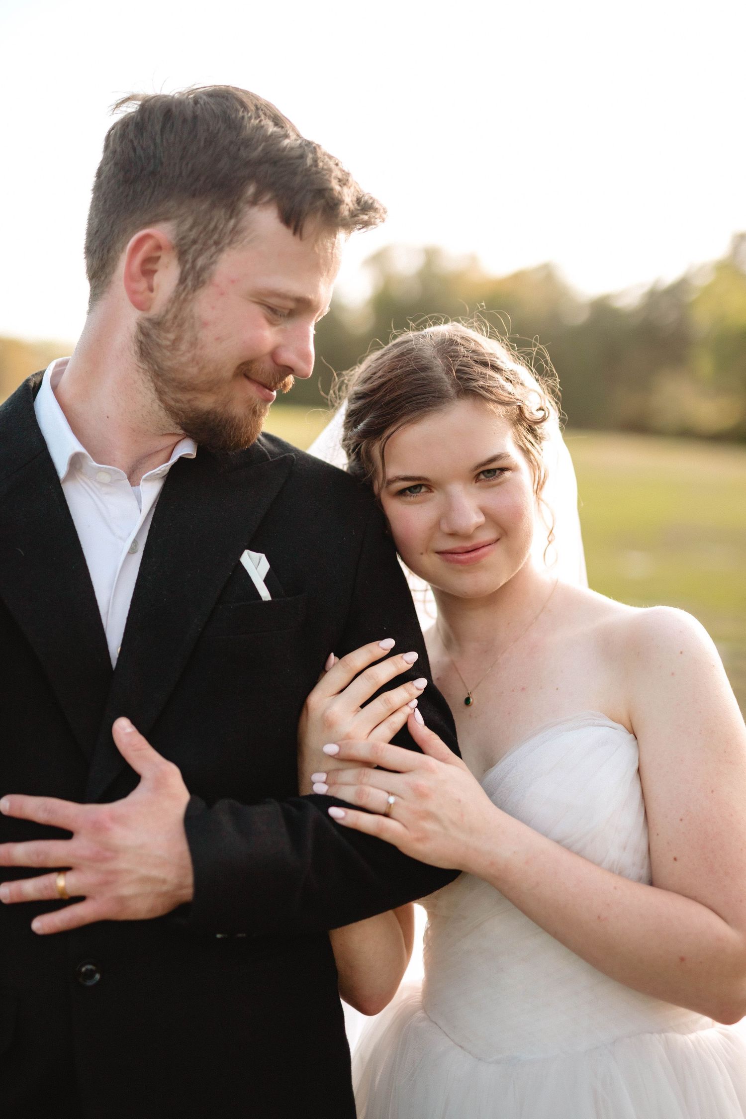 Bride and groom embracing at golden hour showing wedding rings in outdoor field setting.