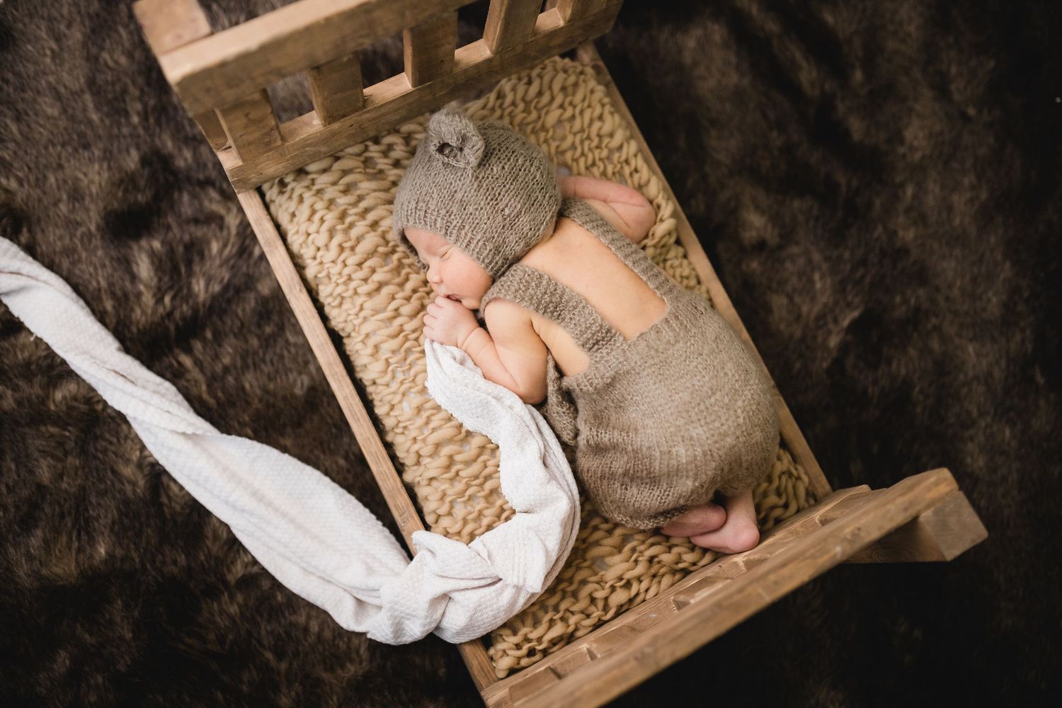 Newborn baby sleeping in tiny wooden bed wearing knit brown bear hat and outfit.