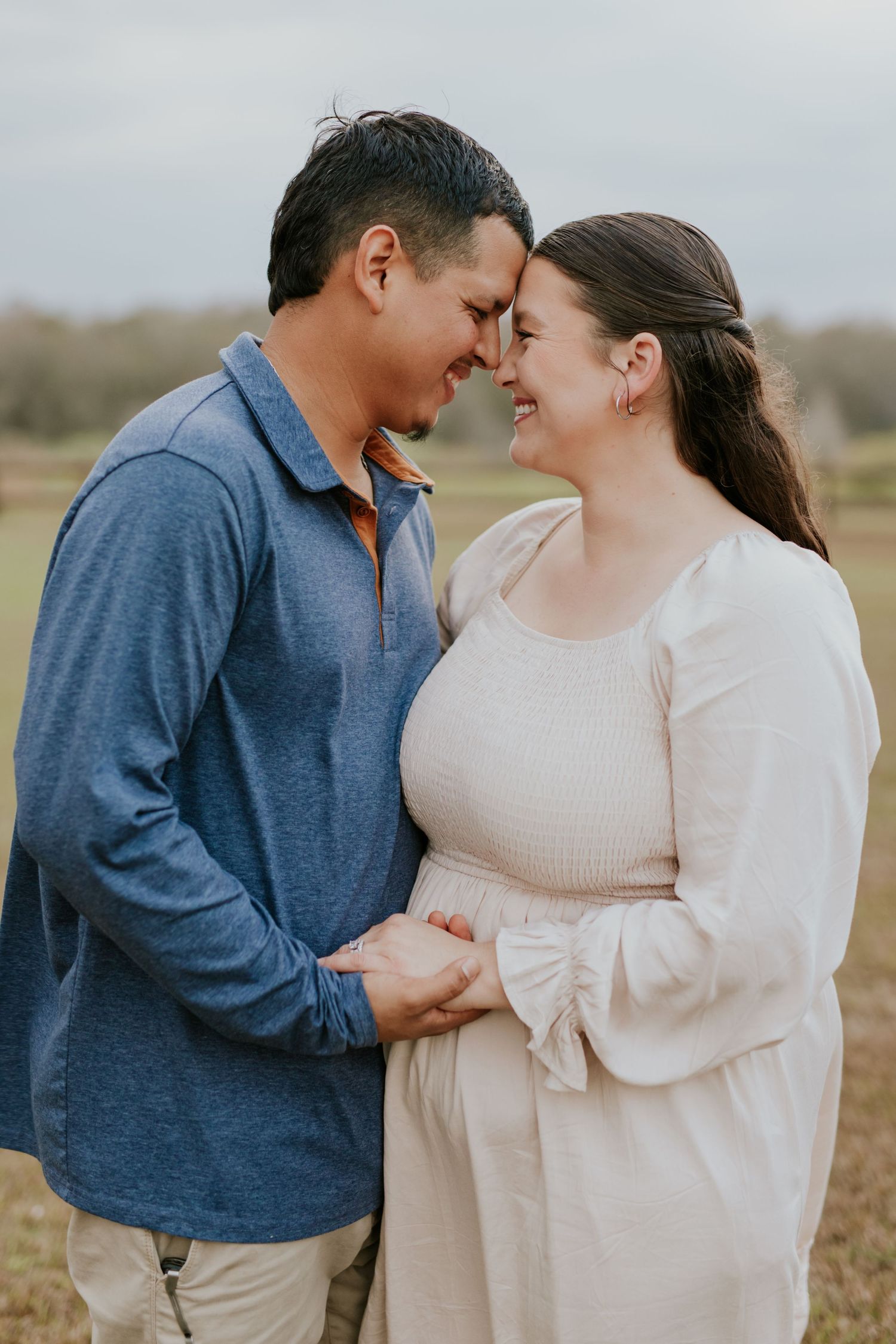 A happy expectant couple touches foreheads tenderly in an outdoor maternity photo session in a field.