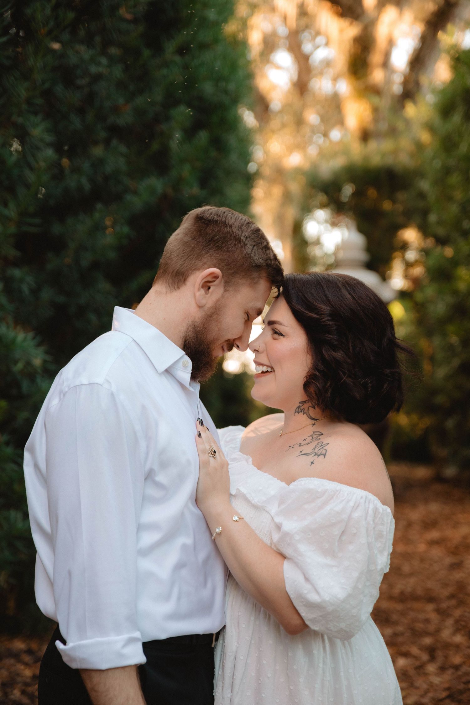 Romantic couple touching foreheads and smiling among tall green hedges at golden hour at Bok Tower Gardens, Lake Wales.