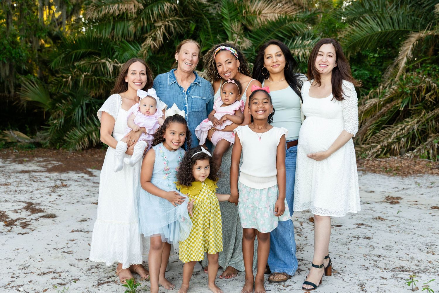 A group of women and young girls smile together outdoors on a white sand beach in Wesley Chapel.