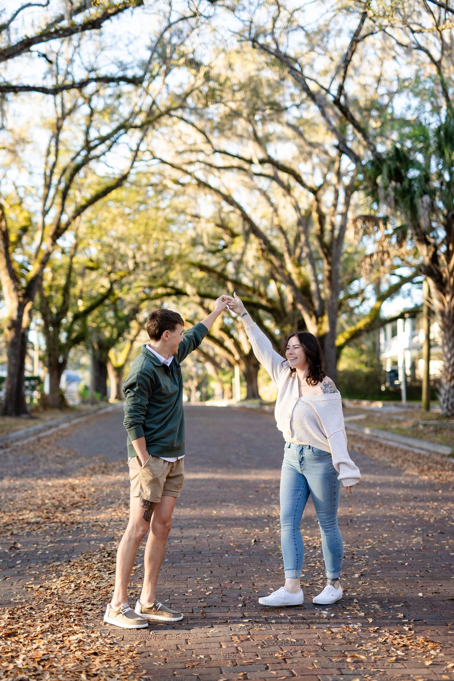 Joyful couple dancing and spinning on a scenic brick road lined with sprawling oak trees.
