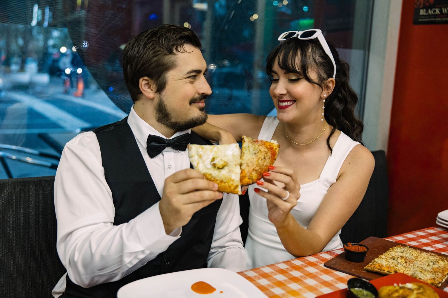 Happy couple in wedding attire sharing pizza slices at a casual restaurant booth in Tampa.