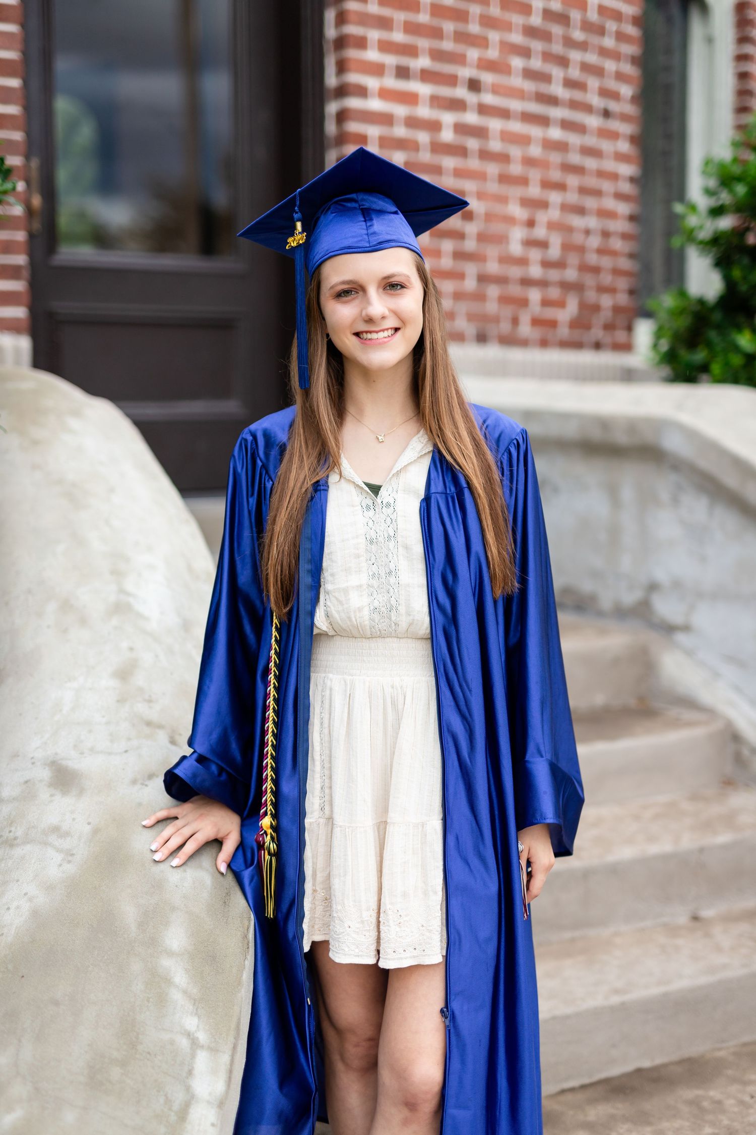 Young woman in blue graduation cap and gown smiling outdoors on brick building steps at the University of Tampa.