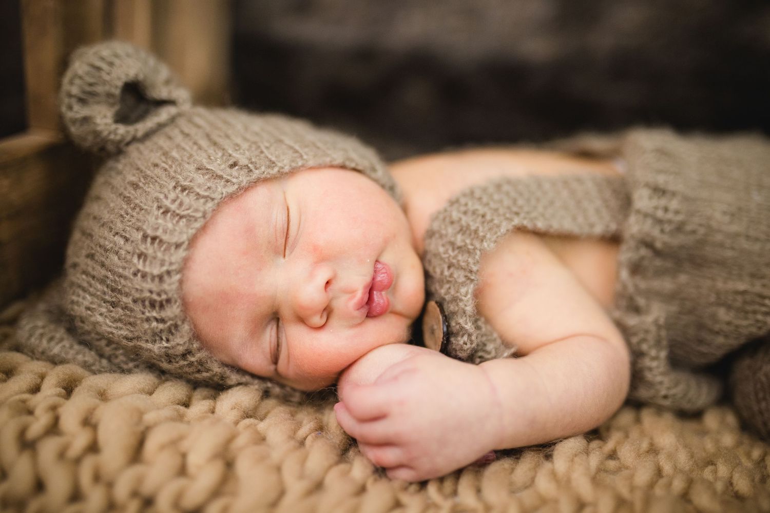 Sleeping newborn baby in knit brown bear hat and outfit on chunky knit blanket.