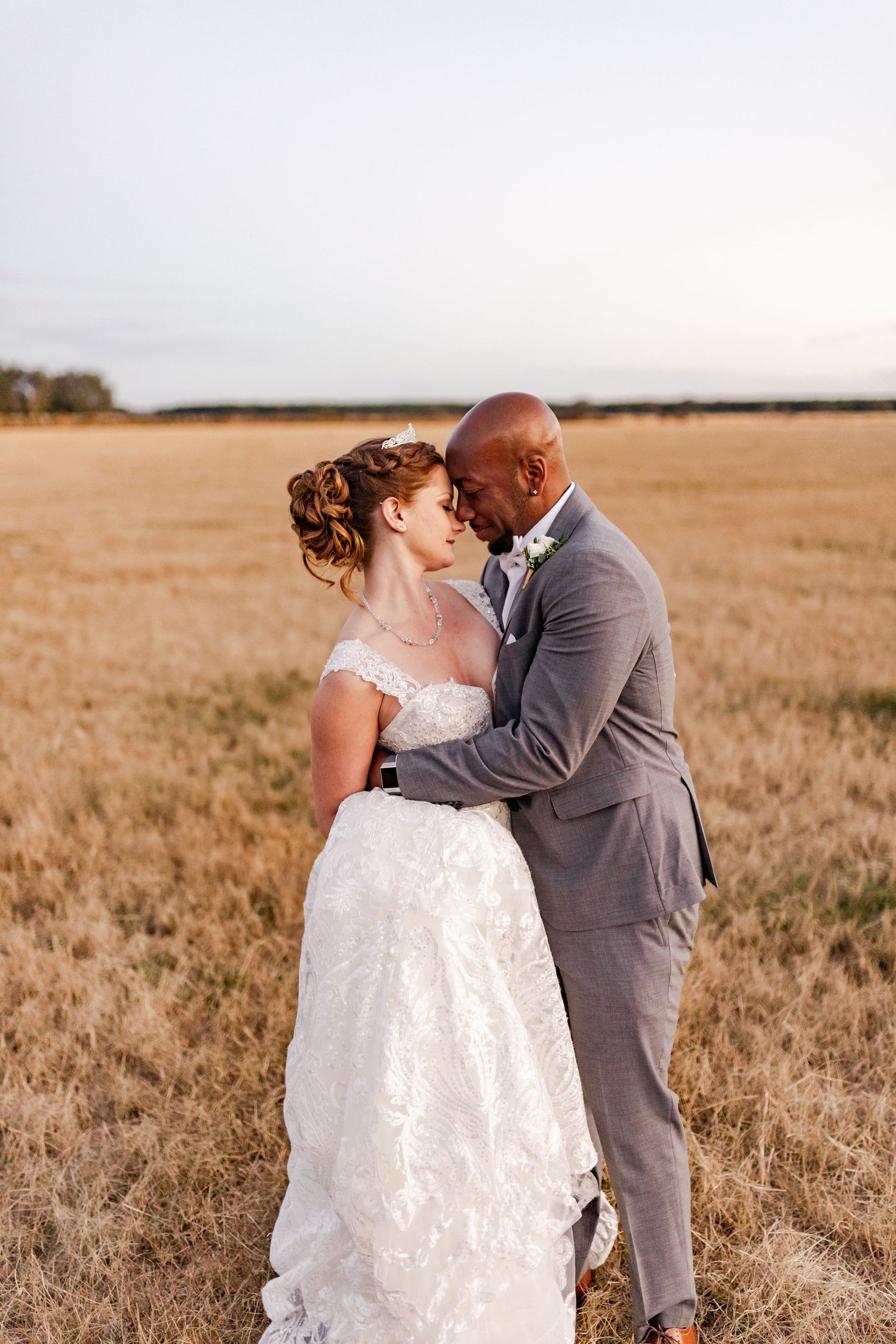 Interracial newlyweds share a tender forehead touch in a golden wheat field at sunset at Legacy Lane.