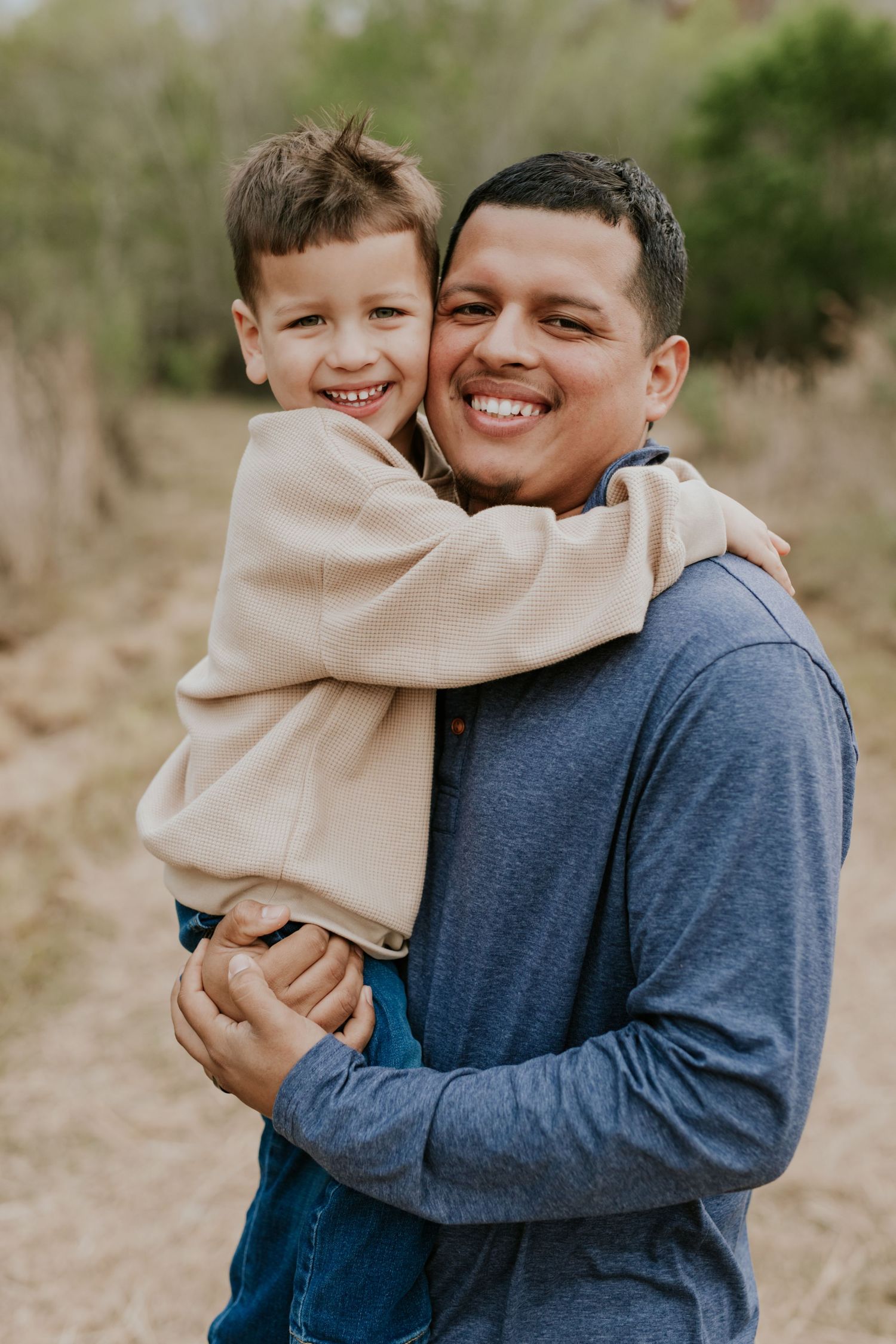 Smiling father and young son share a warm hug on an outdoor nature path.
