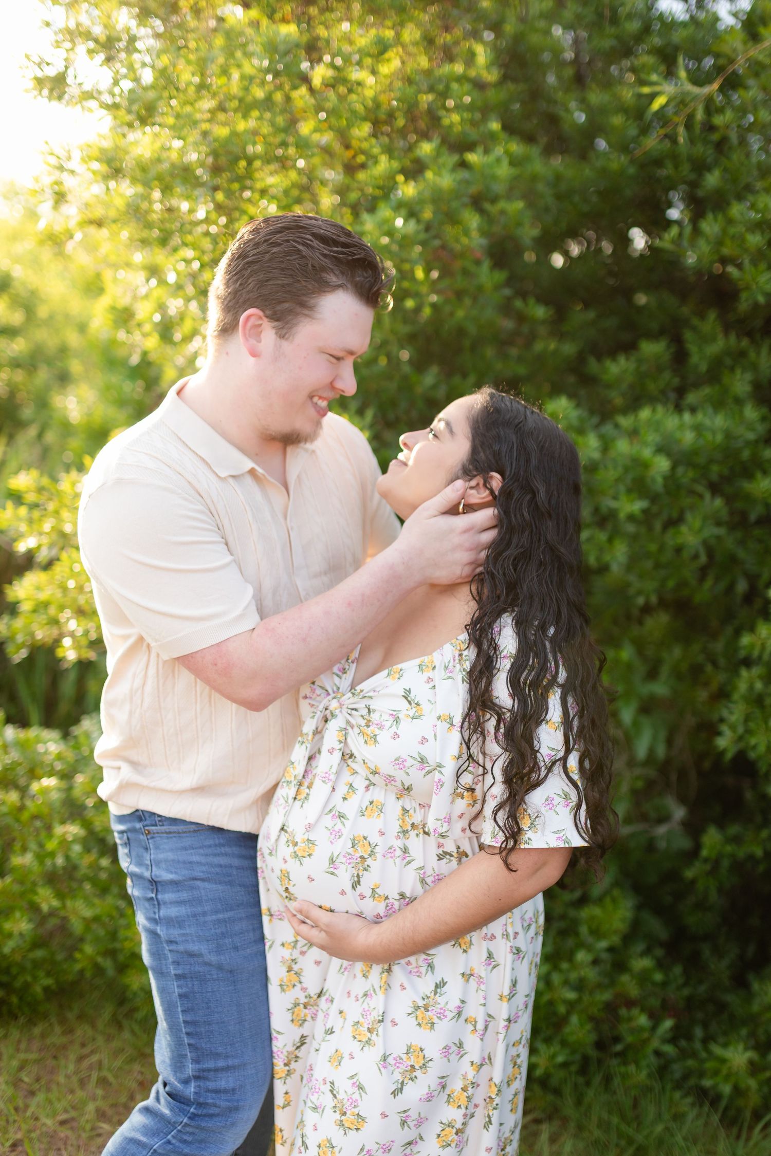 Expectant couple shares tender moment outdoors at golden hour, man gently touches woman's face.