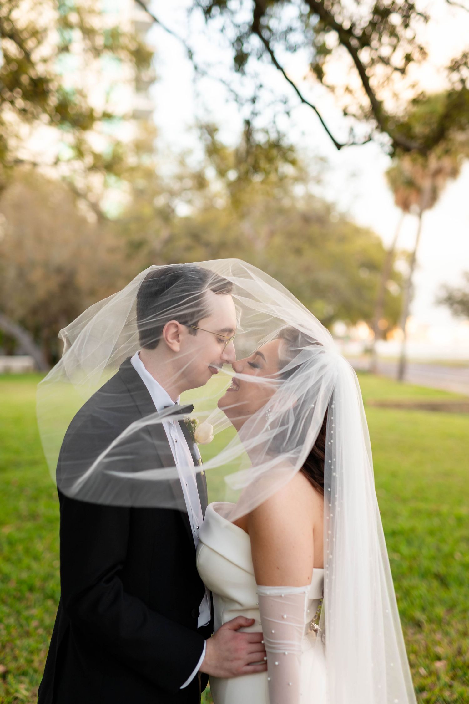 Bride and groom share romantic moment under flowing veil in golden outdoor light in Tampa at the Tampa Garden Club.