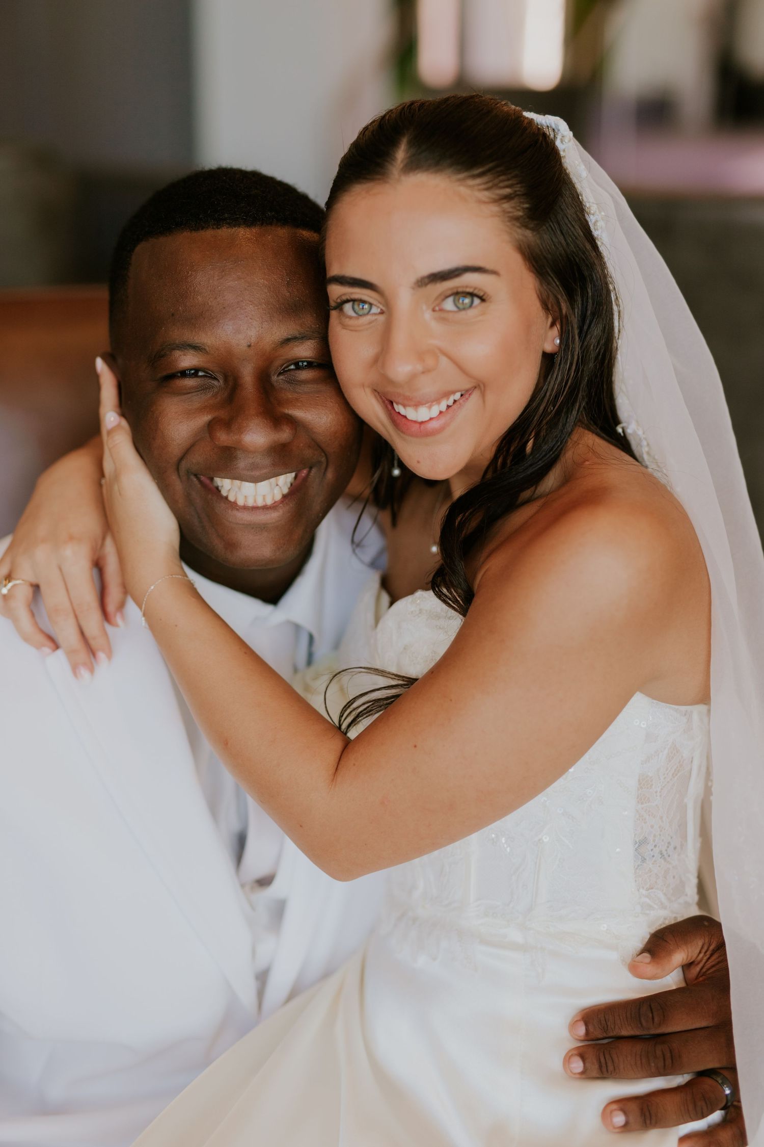 Joyful interracial newlywed couple embrace and smile together in a bright indoor setting.