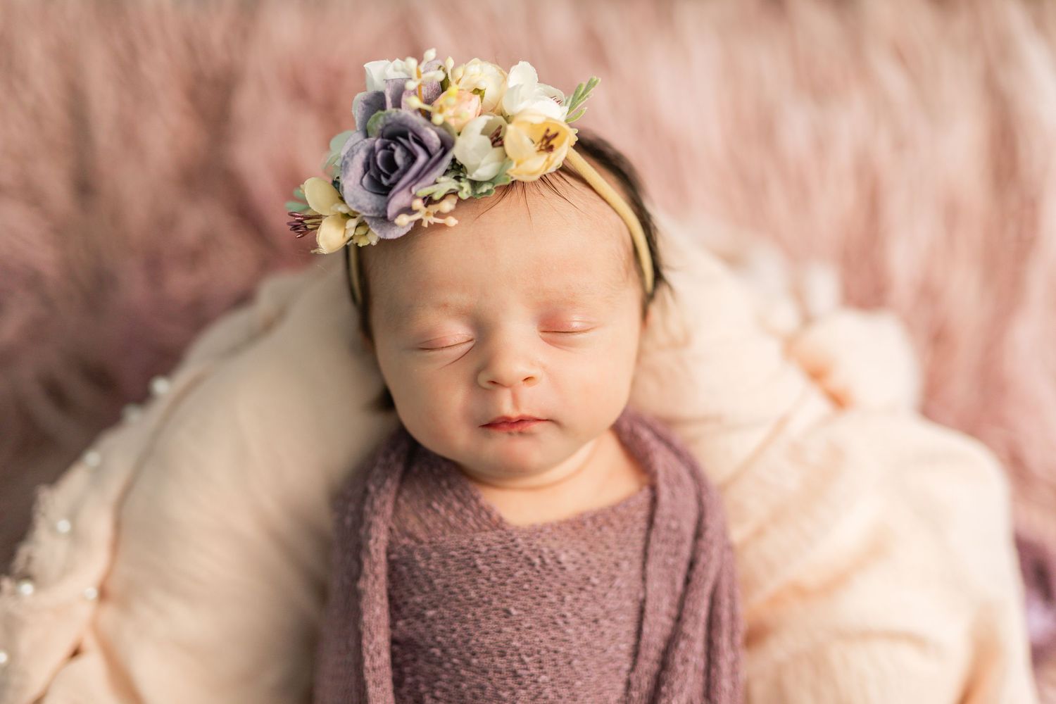 Sleeping newborn baby girl wrapped in purple with a delicate floral crown headband.