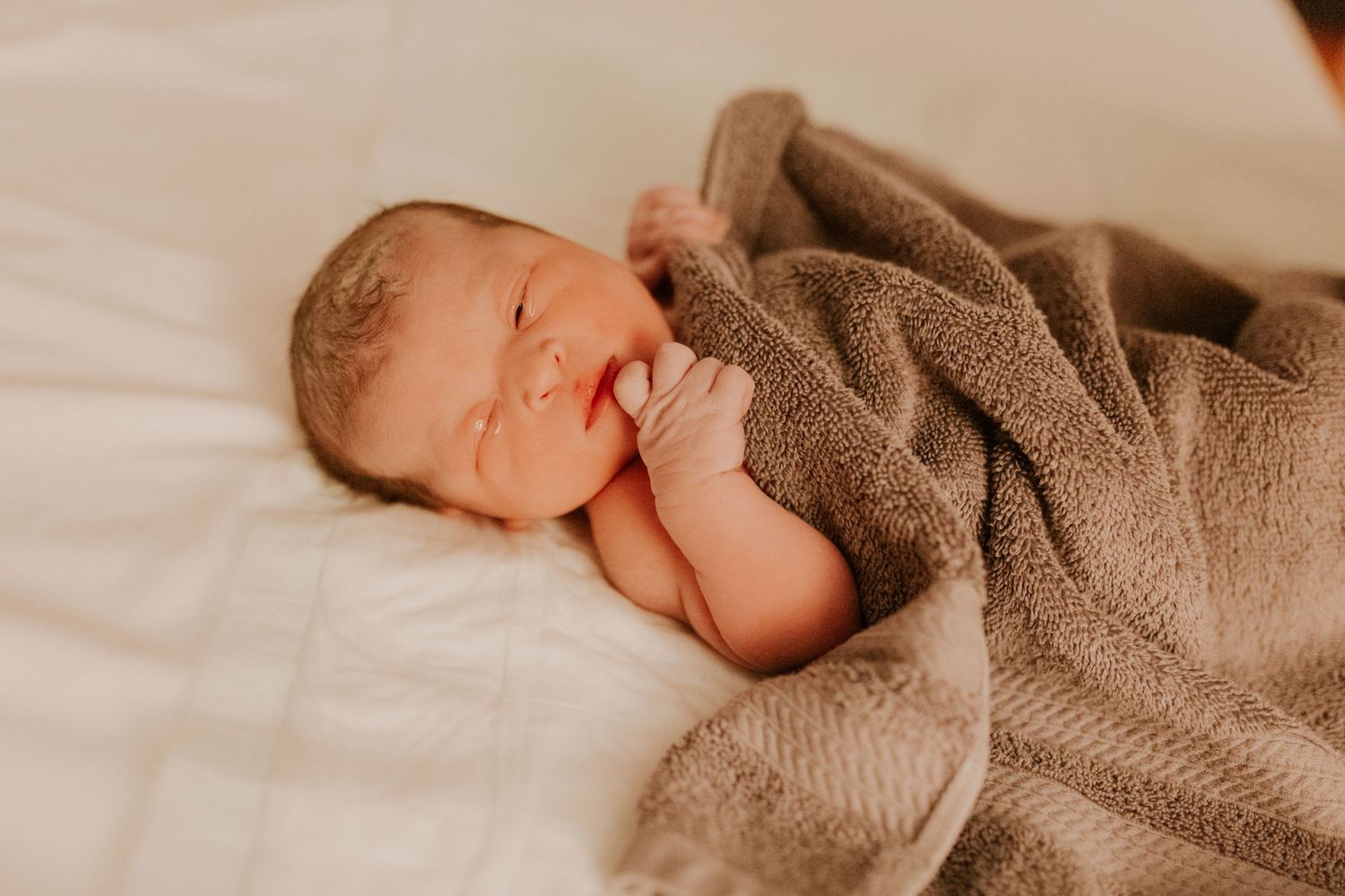 Peaceful newborn baby sleeping wrapped in a soft brown knit blanket.