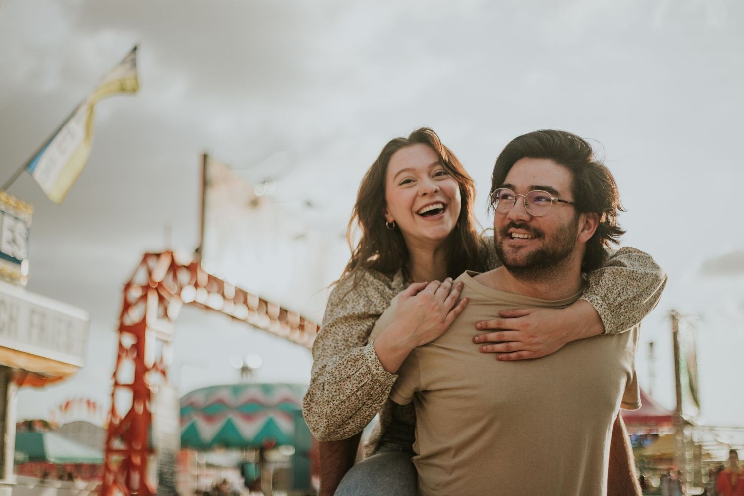 Happy couple shares a piggyback ride and laughs together at a colorful outdoor carnival.