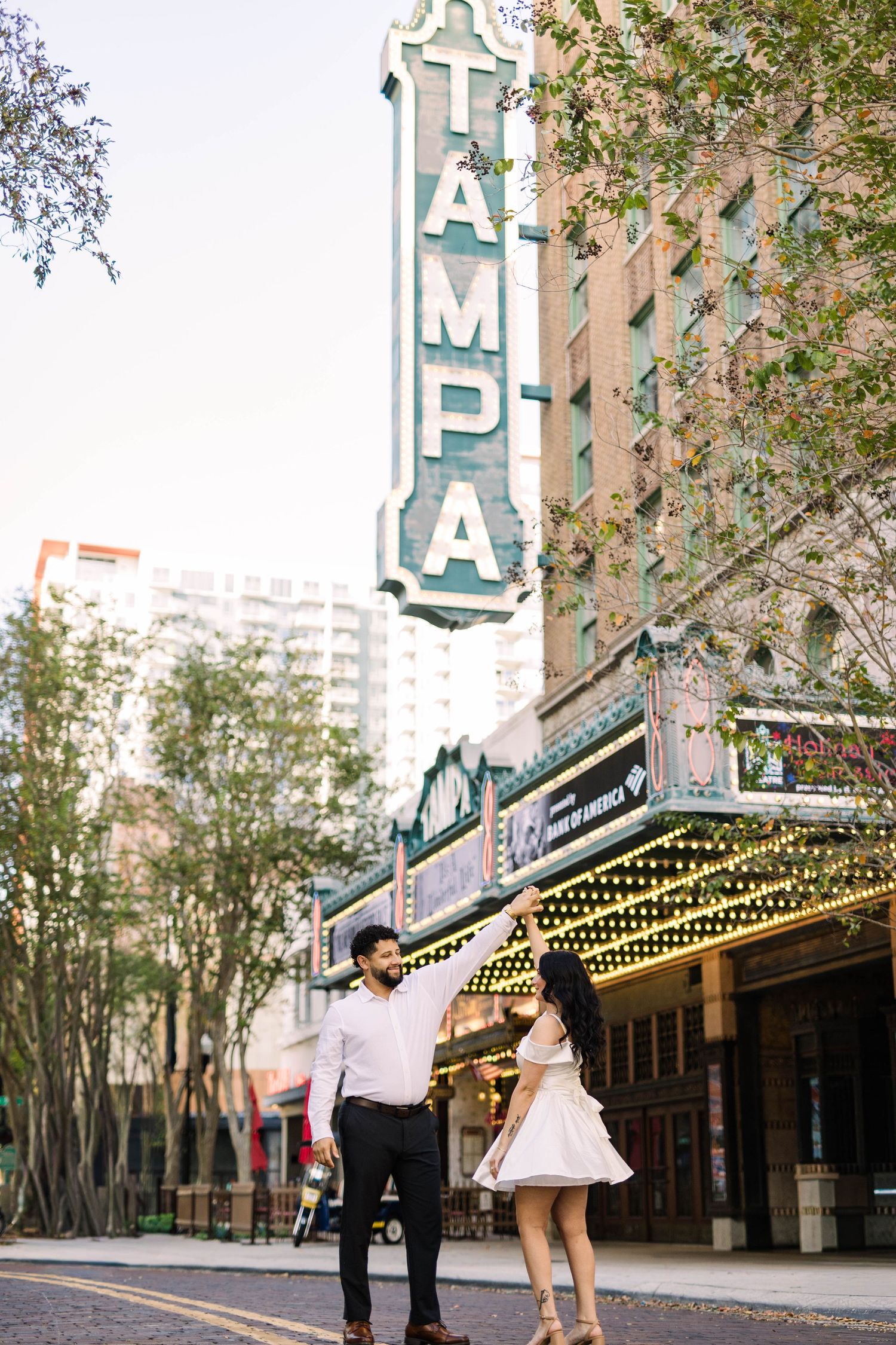 Couple dancing joyfully beneath the iconic illuminated Tampa Theatre marquee sign downtown.
