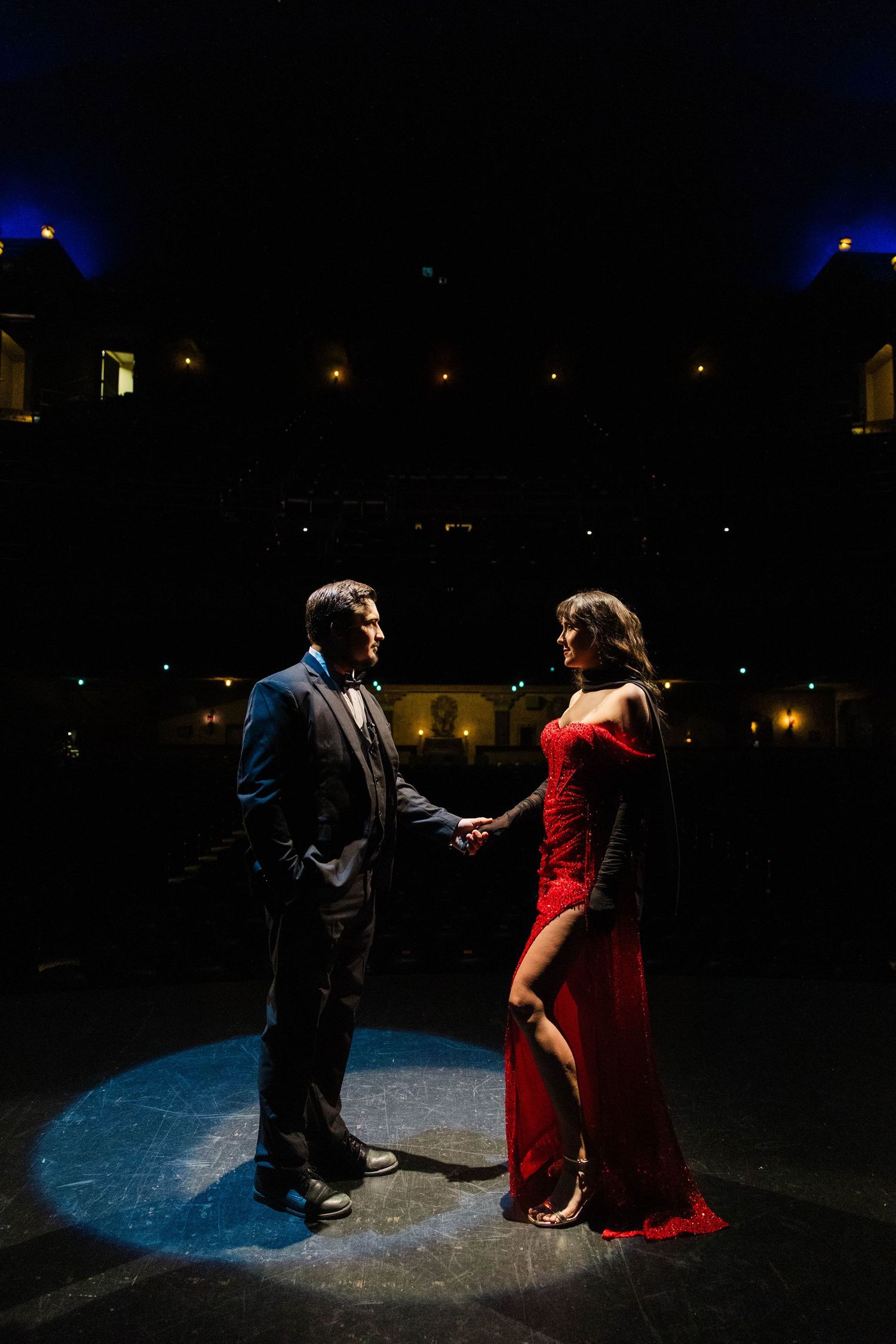 Couple in formal red and black attire hold hands on dark theater stage spotlight at the Tampa Theatre.