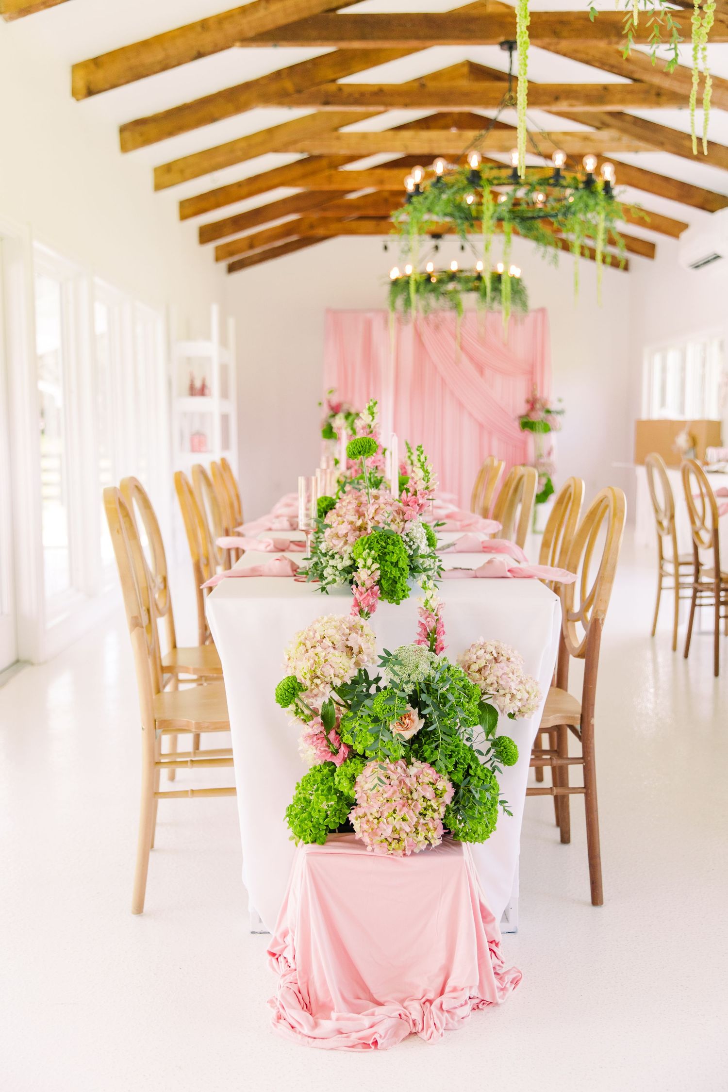 Elegant wedding reception hall with long tables adorned with pink and green floral arrangements at the Colonial at Sunset.