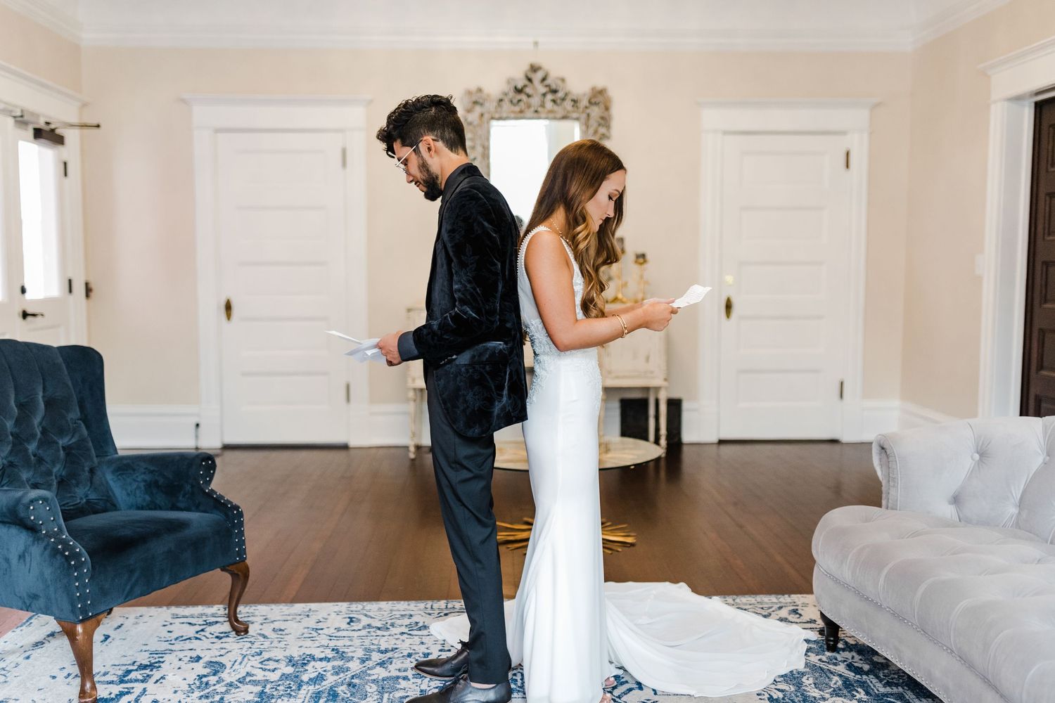 Bride and groom standing back to back reading private vow letters before wedding ceremony indoors at The Orlo.