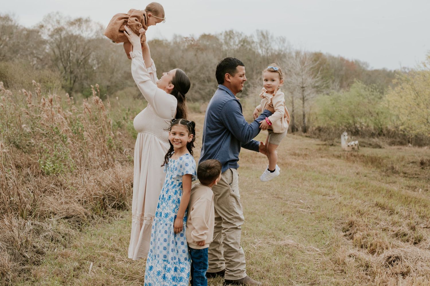 Playful family of six enjoys outdoor time in a scenic field with tall grass.