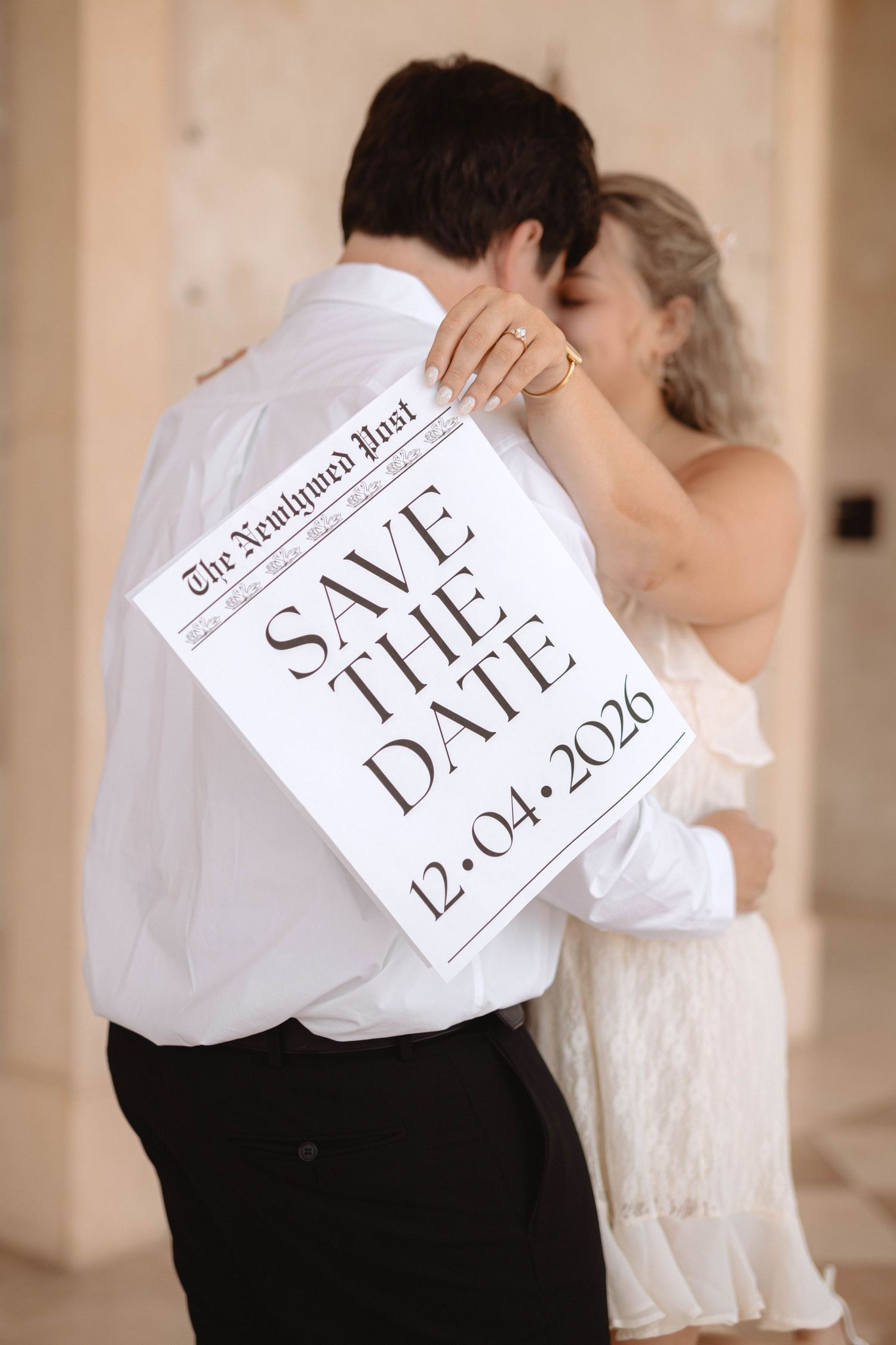 Engaged couple kissing while holding a Save the Date sign for December 4, 2026.