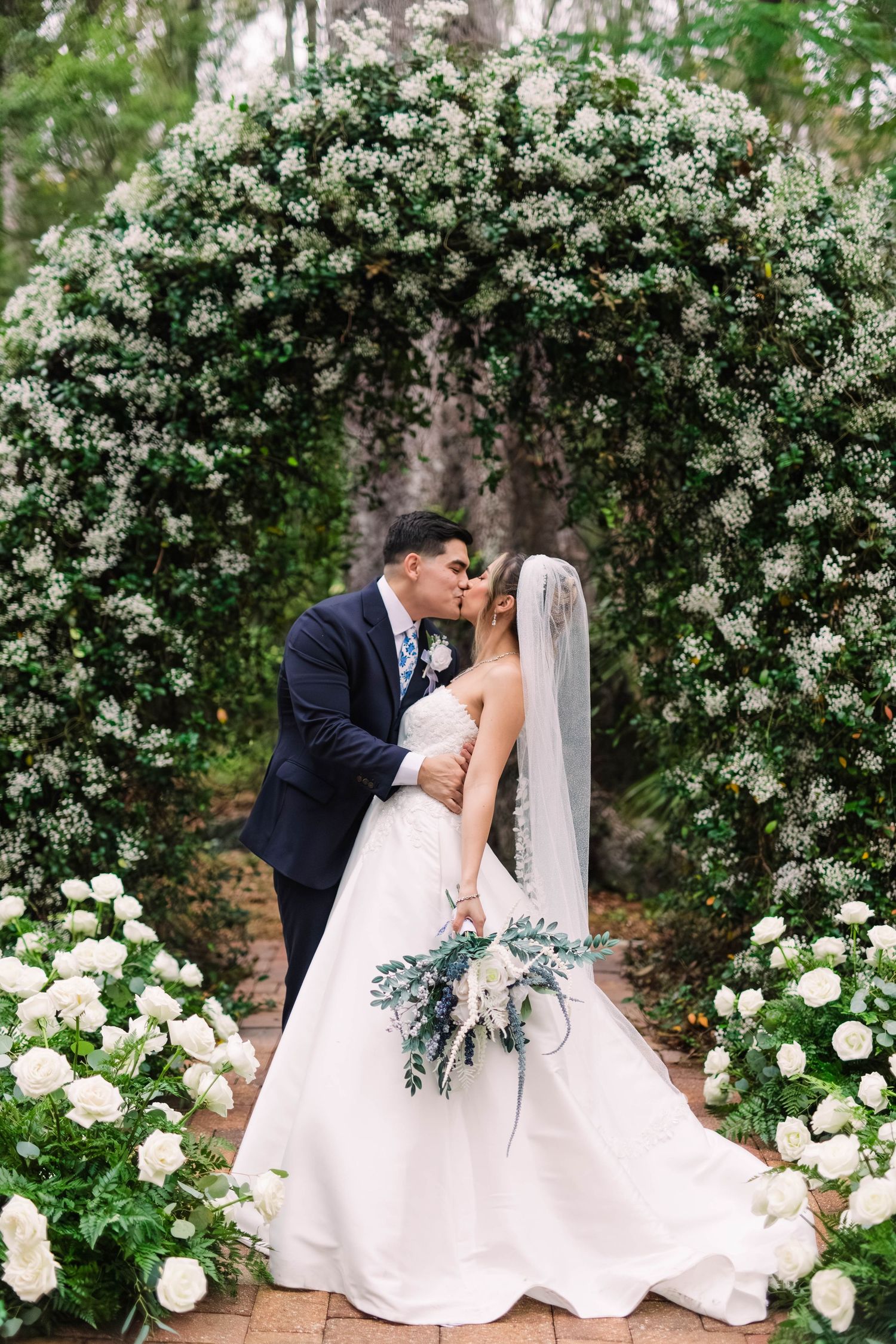 Bride and groom kissing under a stunning floral arch adorned with white flowers and greenery.