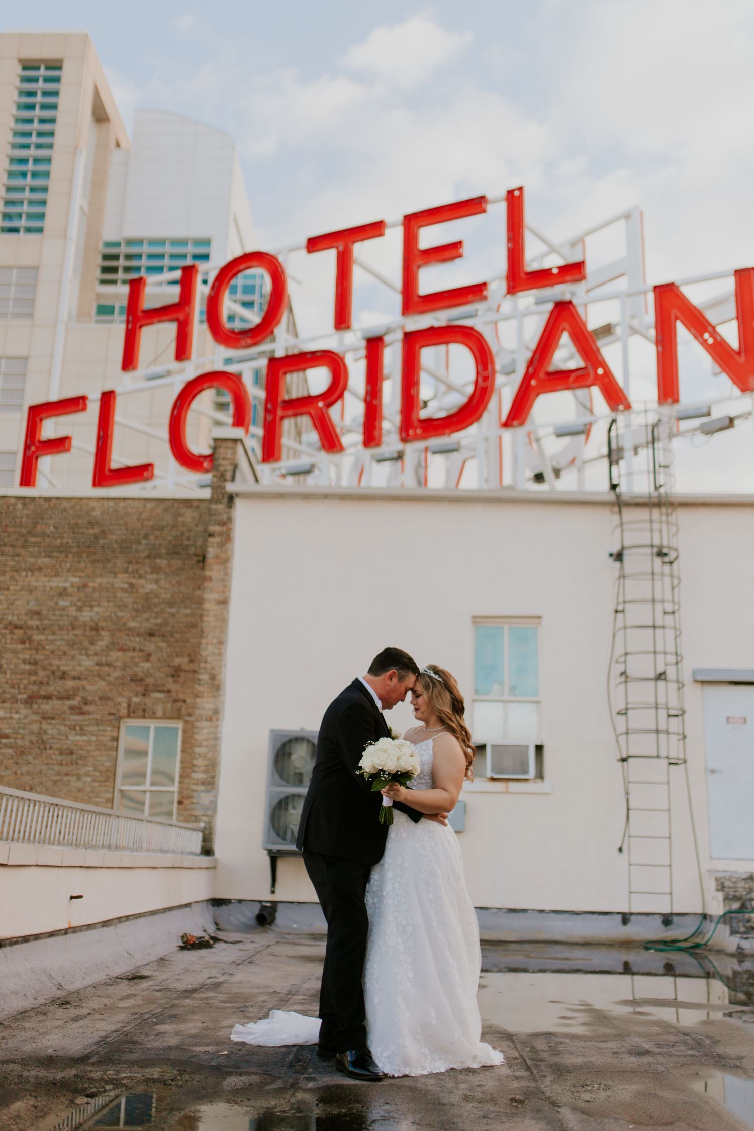 Bride and groom share a tender kiss on rooftop beneath iconic Hotel Floridan neon sign in Tampa.
