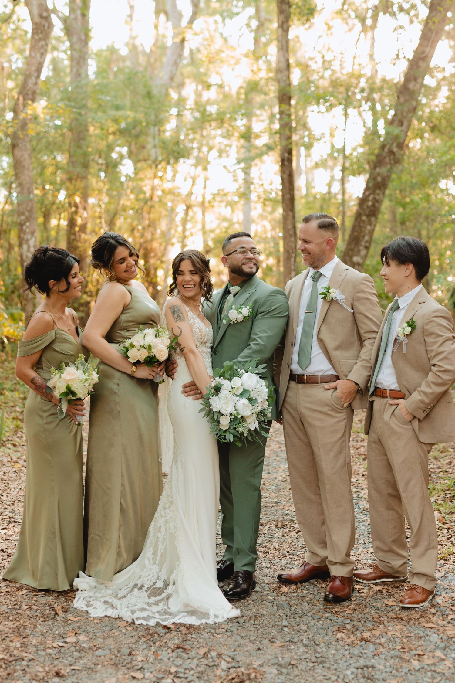 Wedding party poses in golden forest light, bridesmaids in sage green dresses and groomsmen in khaki suits.