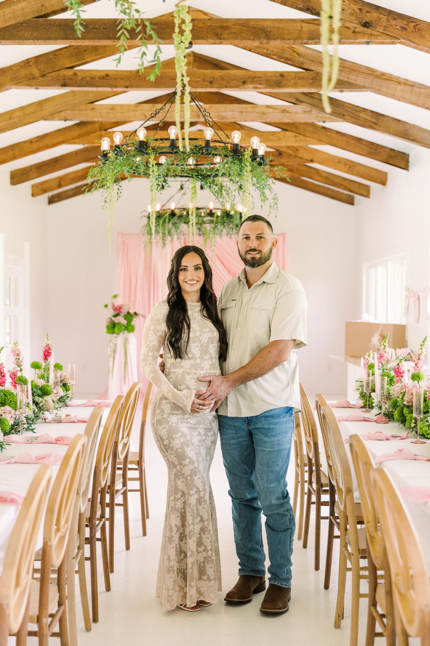 Expecting couple posing in elegant pink-decorated event hall with wooden beam ceiling at the Colonial at Sunset..