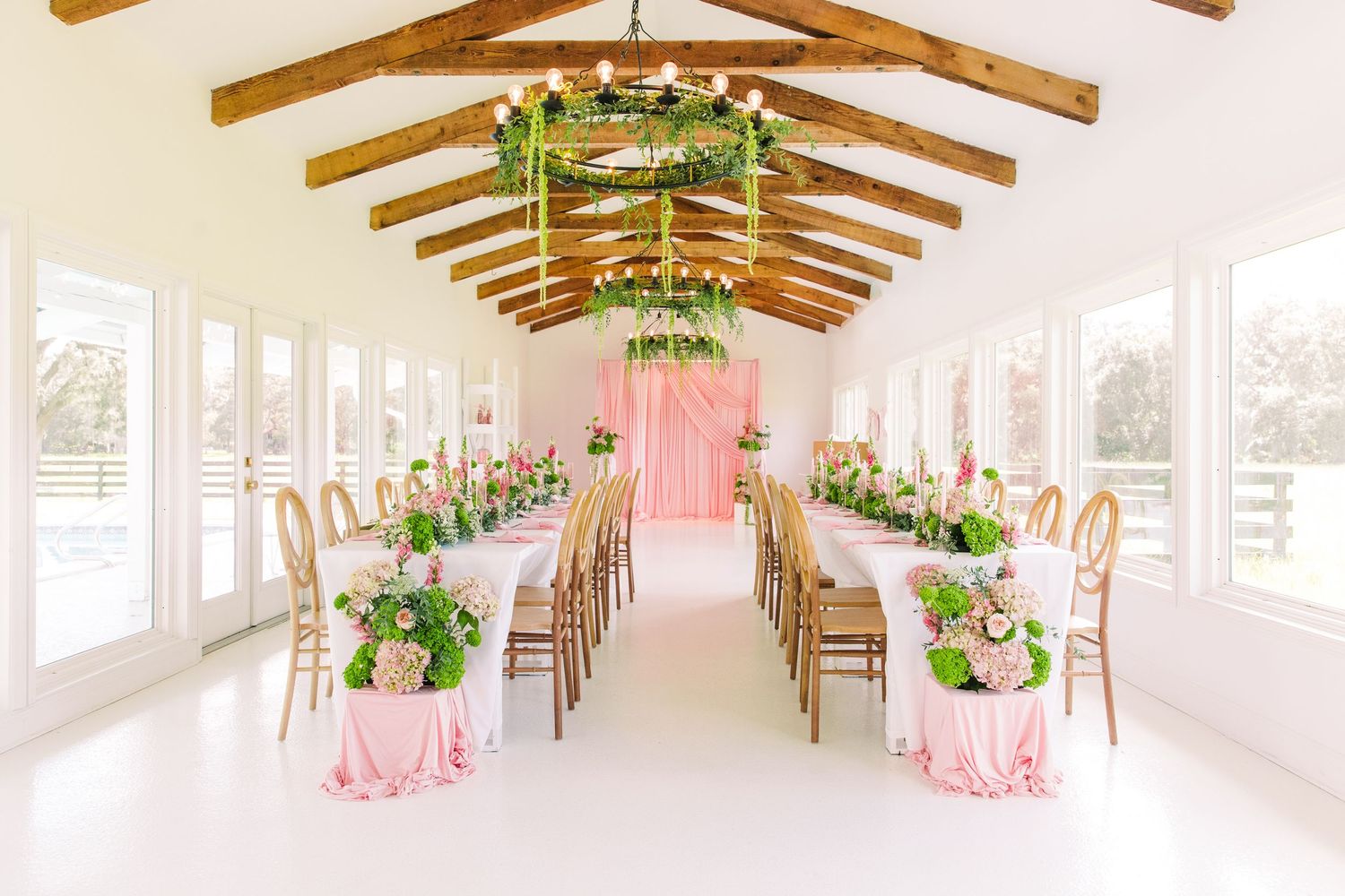 Bright wedding venue with vaulted wood beam ceiling, pink draped altar, floral centerpieces, and gold chairs at The Colonial at Sunset.