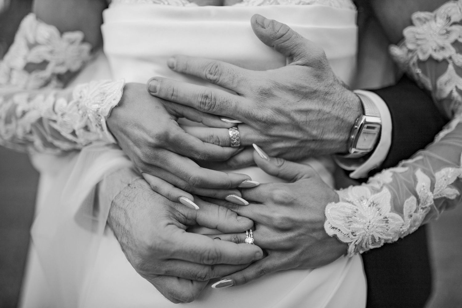 Black and white close-up of bride and groom hands with wedding rings embracing at their ceremony.