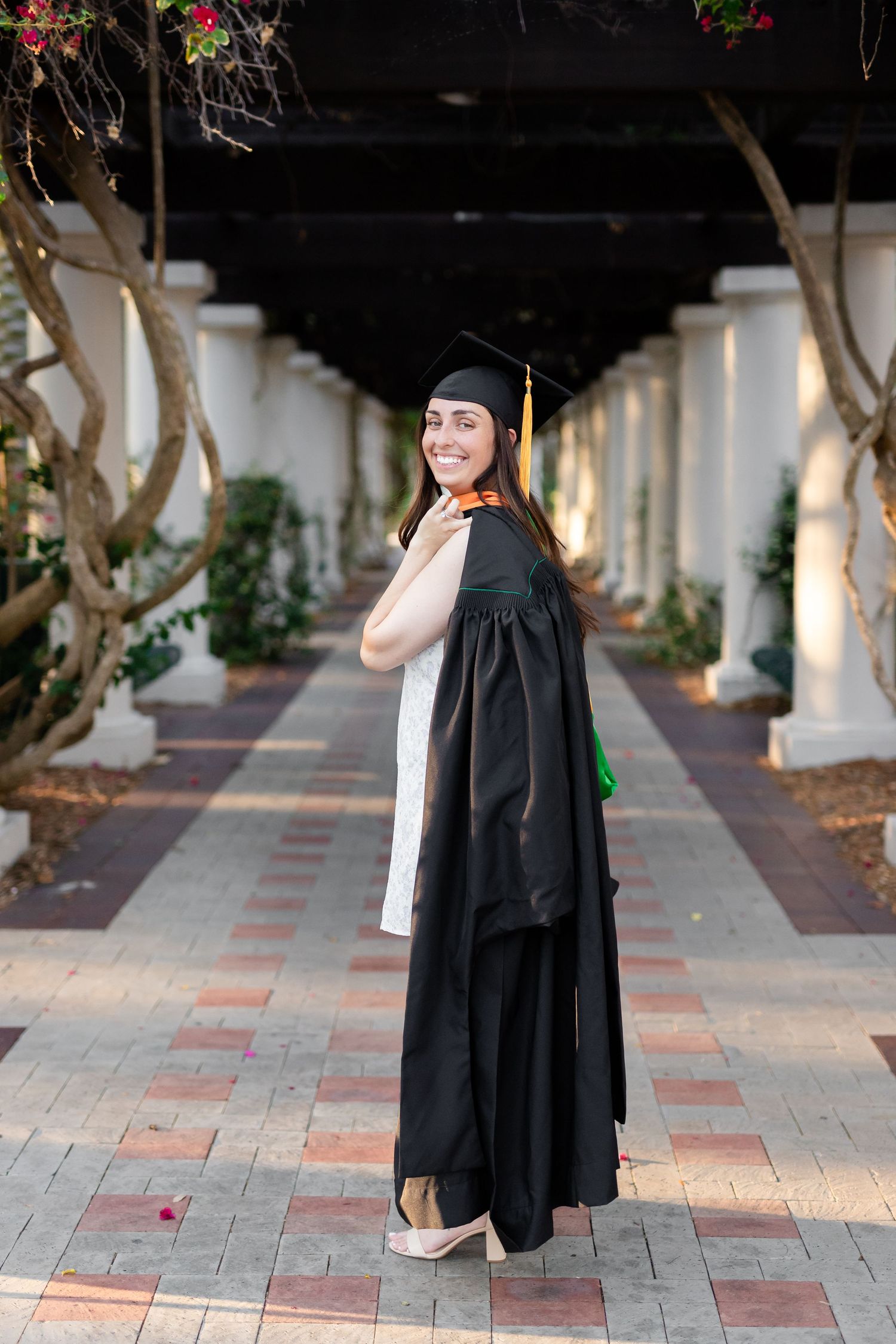 Female graduate in black cap and gown smiling over shoulder in elegant columned outdoor walkway at the University of South Florida.