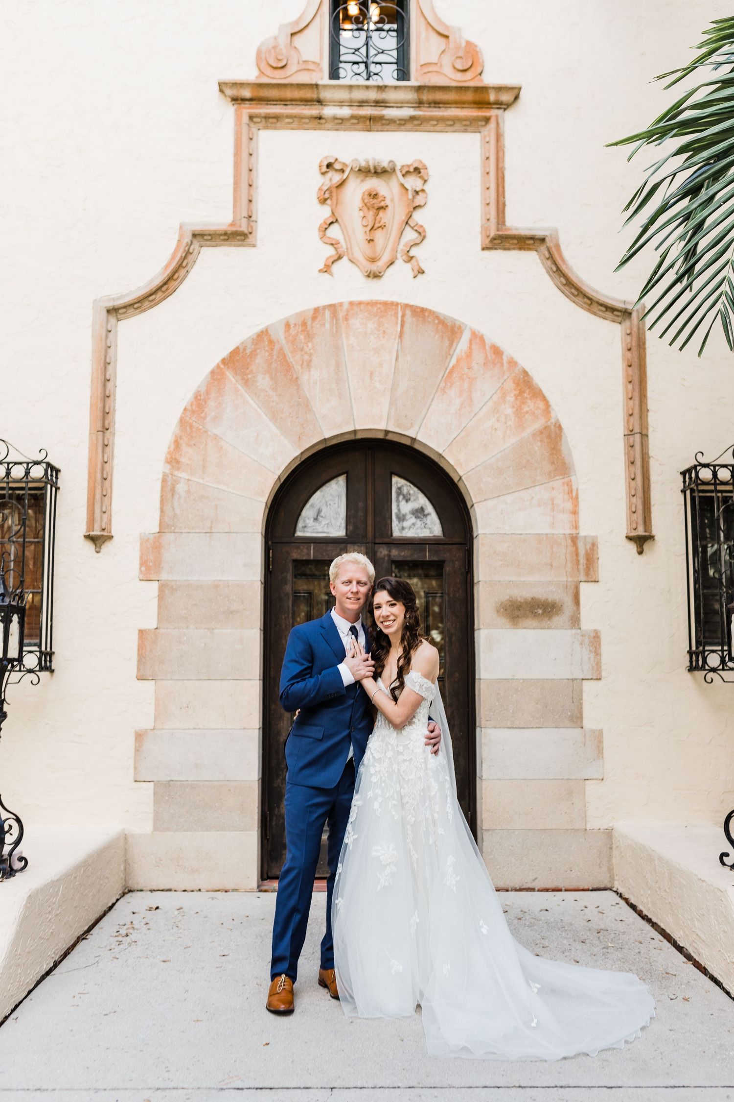 Bride and groom pose before an ornate arched doorway of a Spanish-style wedding venue at Powel Crosley Estate, Sarasota.