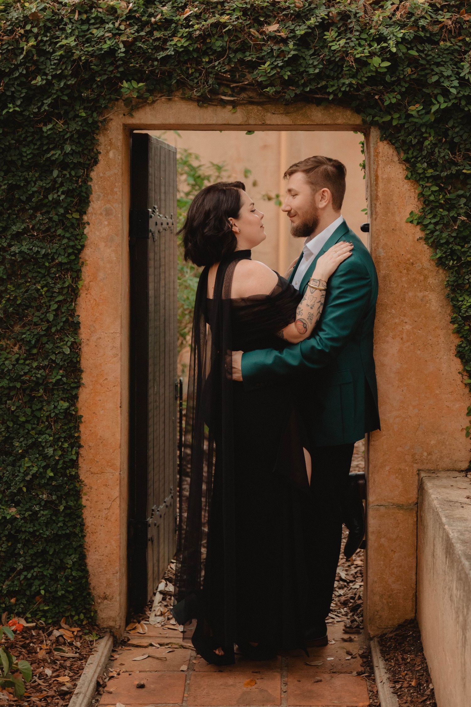 Couple in formal wear embracing in ivy-covered stone doorway in romantic outdoor setting at Bok Tower Gardens, Lake Wales.