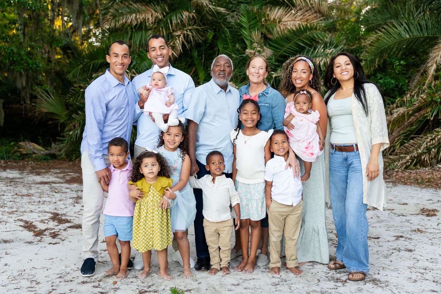 A multigenerational family with children poses together on a sandy beach with tropical greenery in Wesley Chapel.