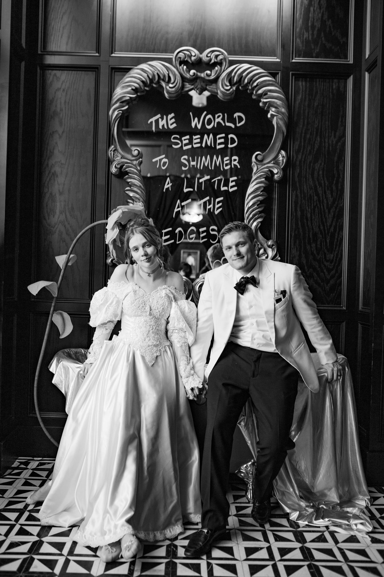 Bride and groom hold hands in black and white wedding portrait beside decorative sign at the Floridan Social, St. Petersburg Florida.