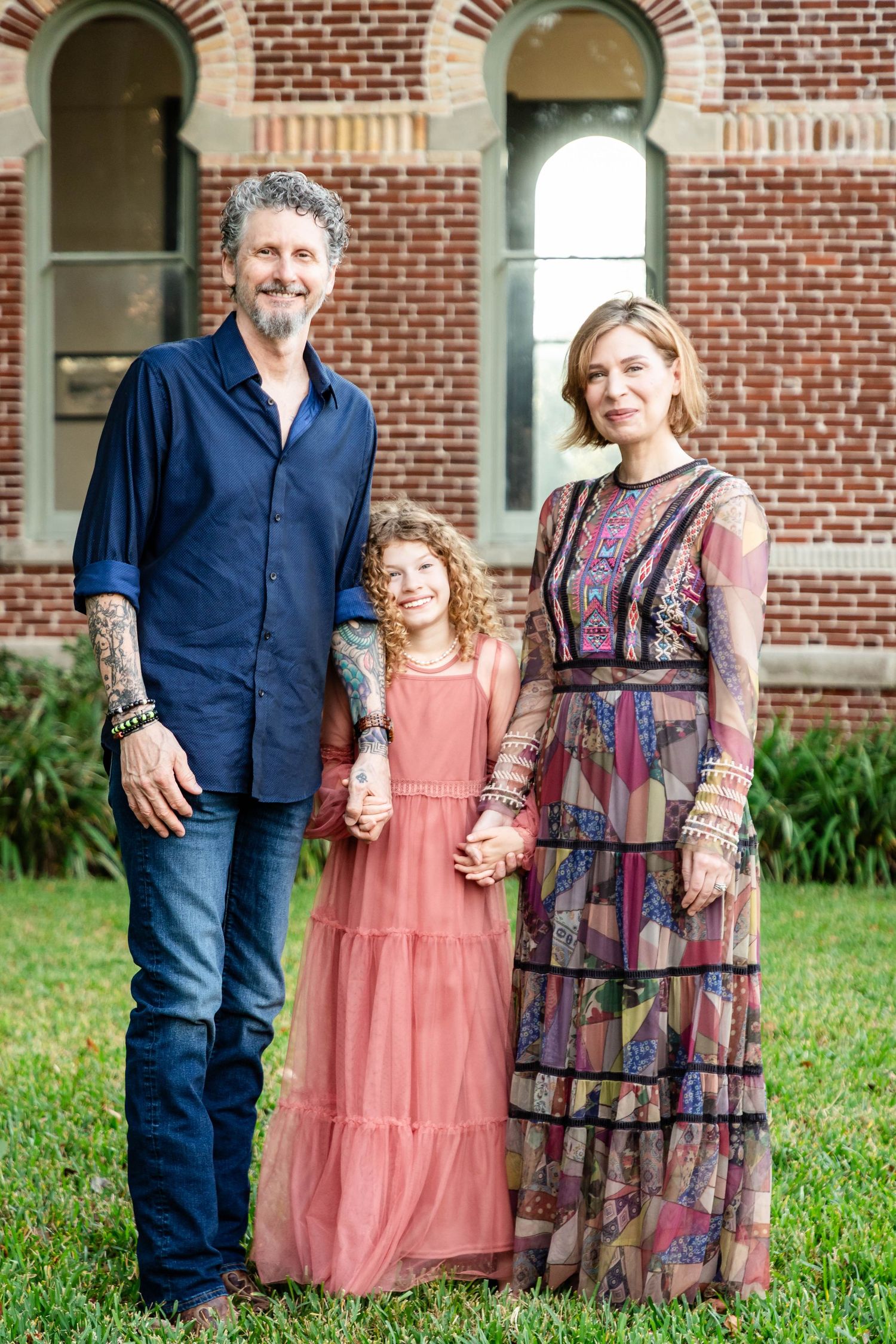 Family of three with tattooed parents and curly-haired daughter posing outside brick building at The University of Tampa.