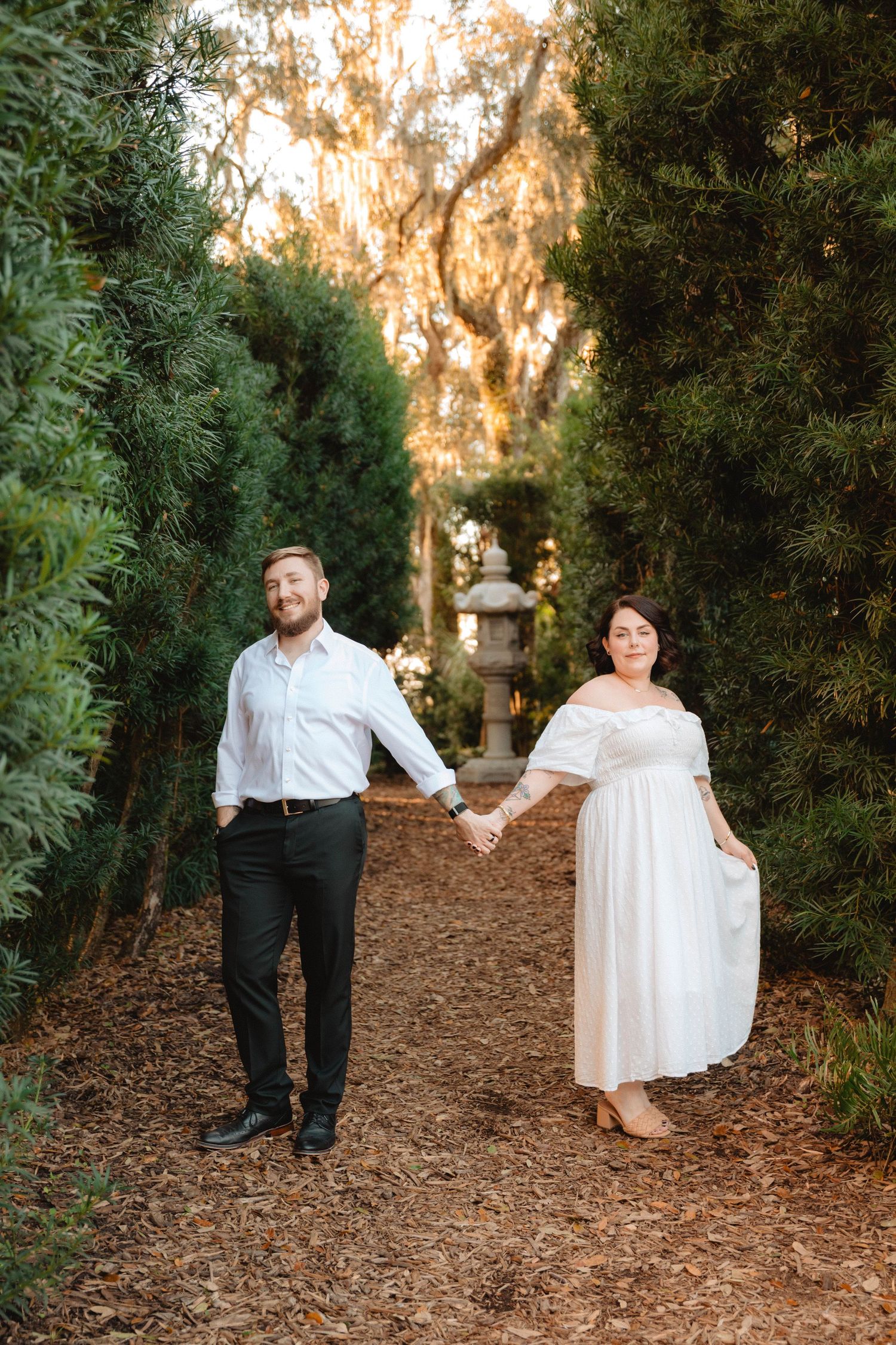 Engaged couple holding hands while walking along a pine needle path between tall hedges at sunset at Bok Tower Gardens, Lake Wales.