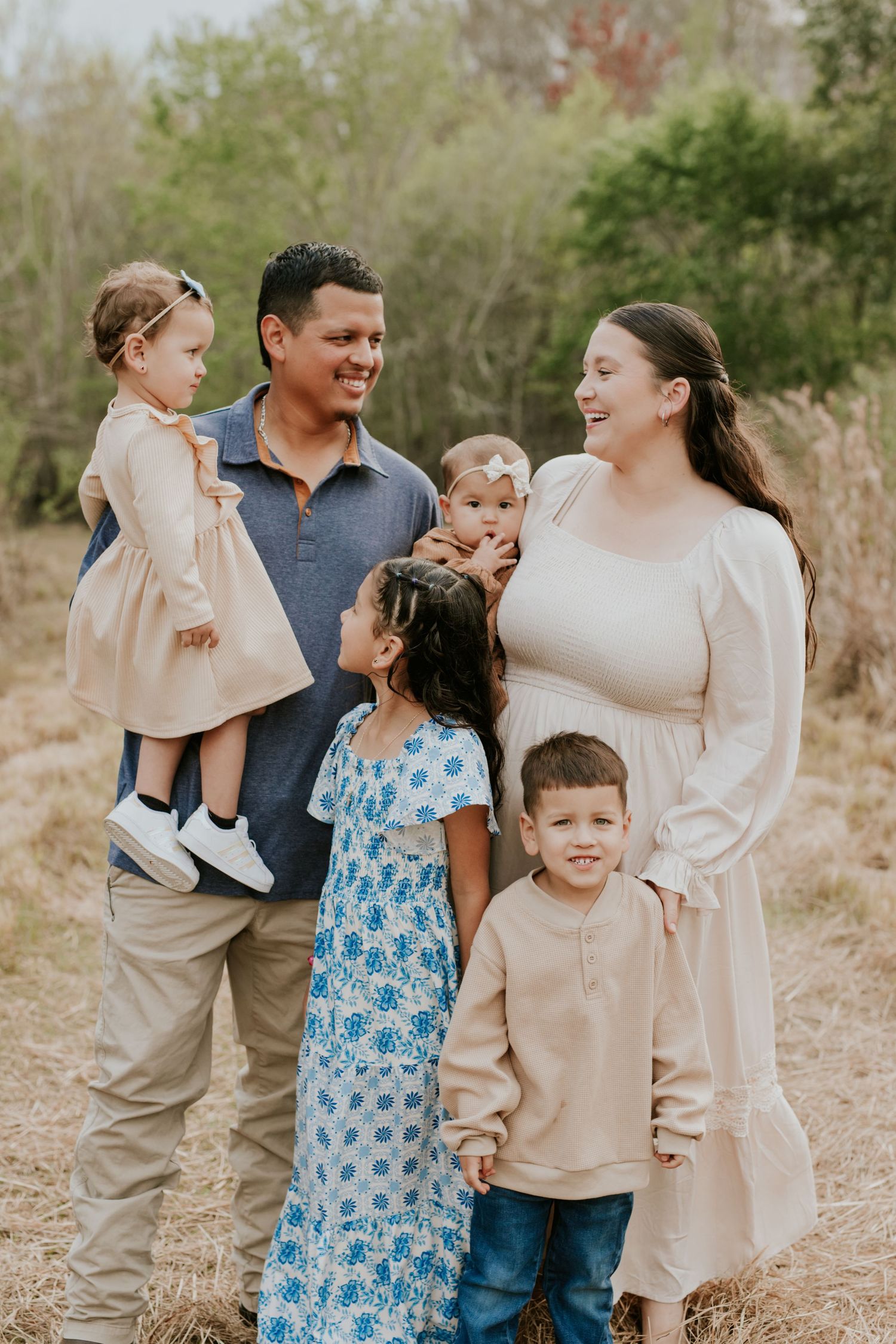 Happy family of six poses together in a natural outdoor field setting.