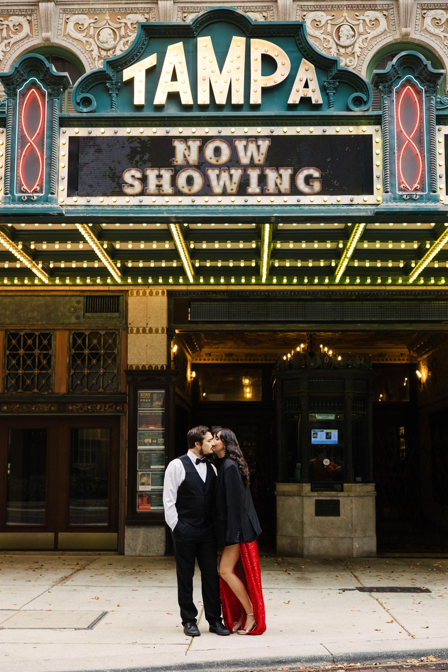 Couple kissing under the iconic Tampa Theatre marquee sign at night with glowing lights.