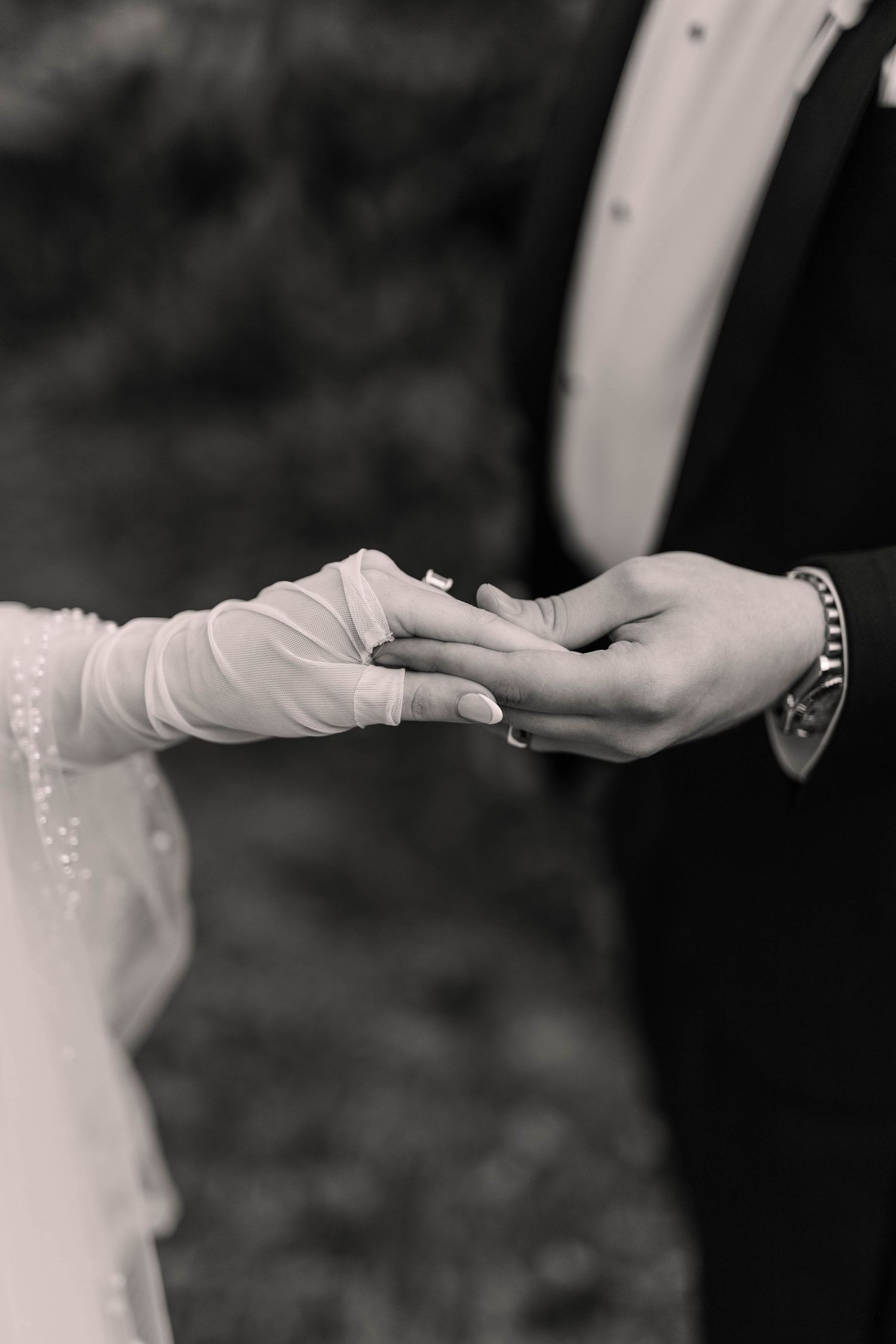 Black and white close-up of bride in lace glove placing wedding ring on grooms hand.
