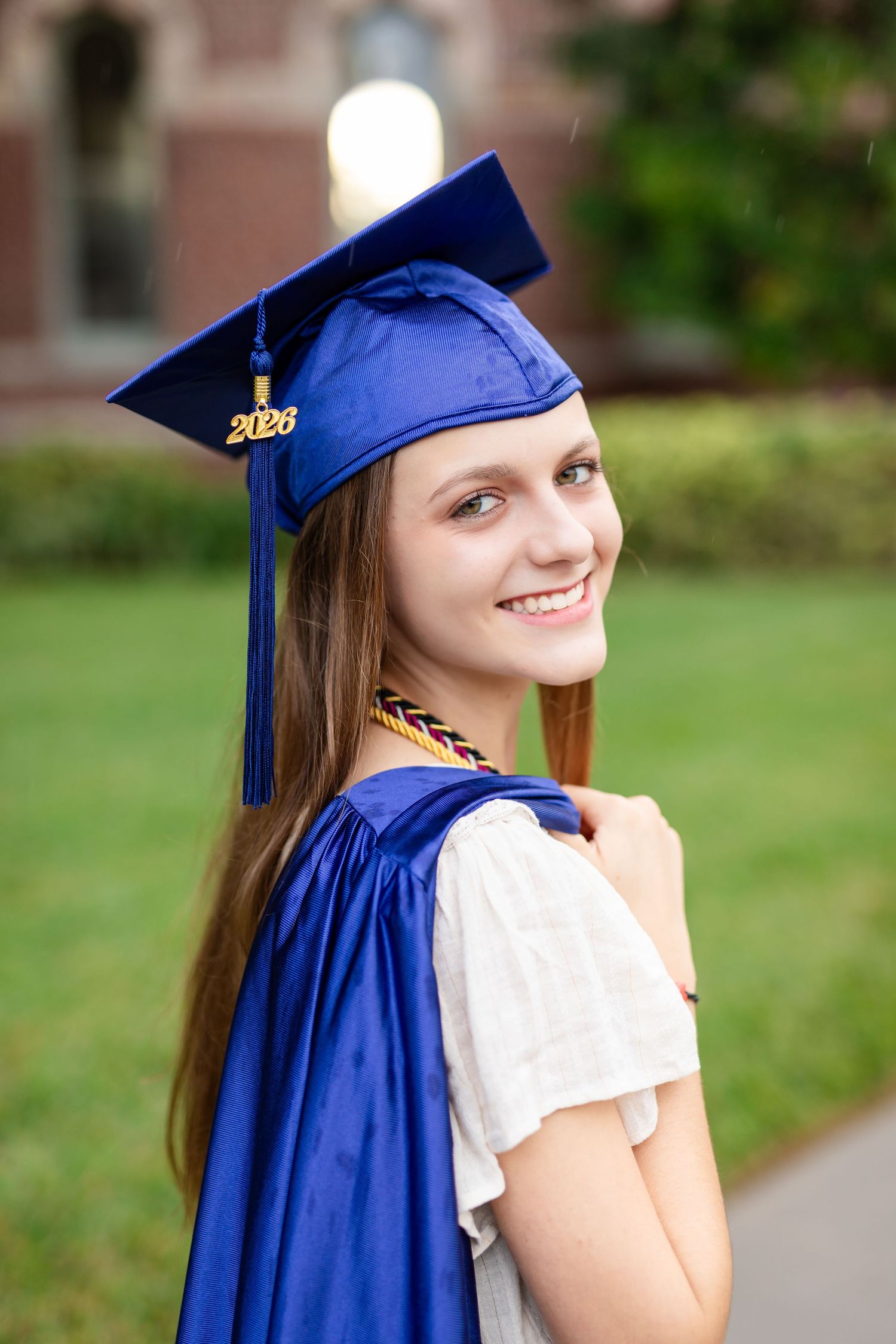 Smiling young woman in blue graduation cap and gown for the class of 2026 outdoors at the University of Tampa.