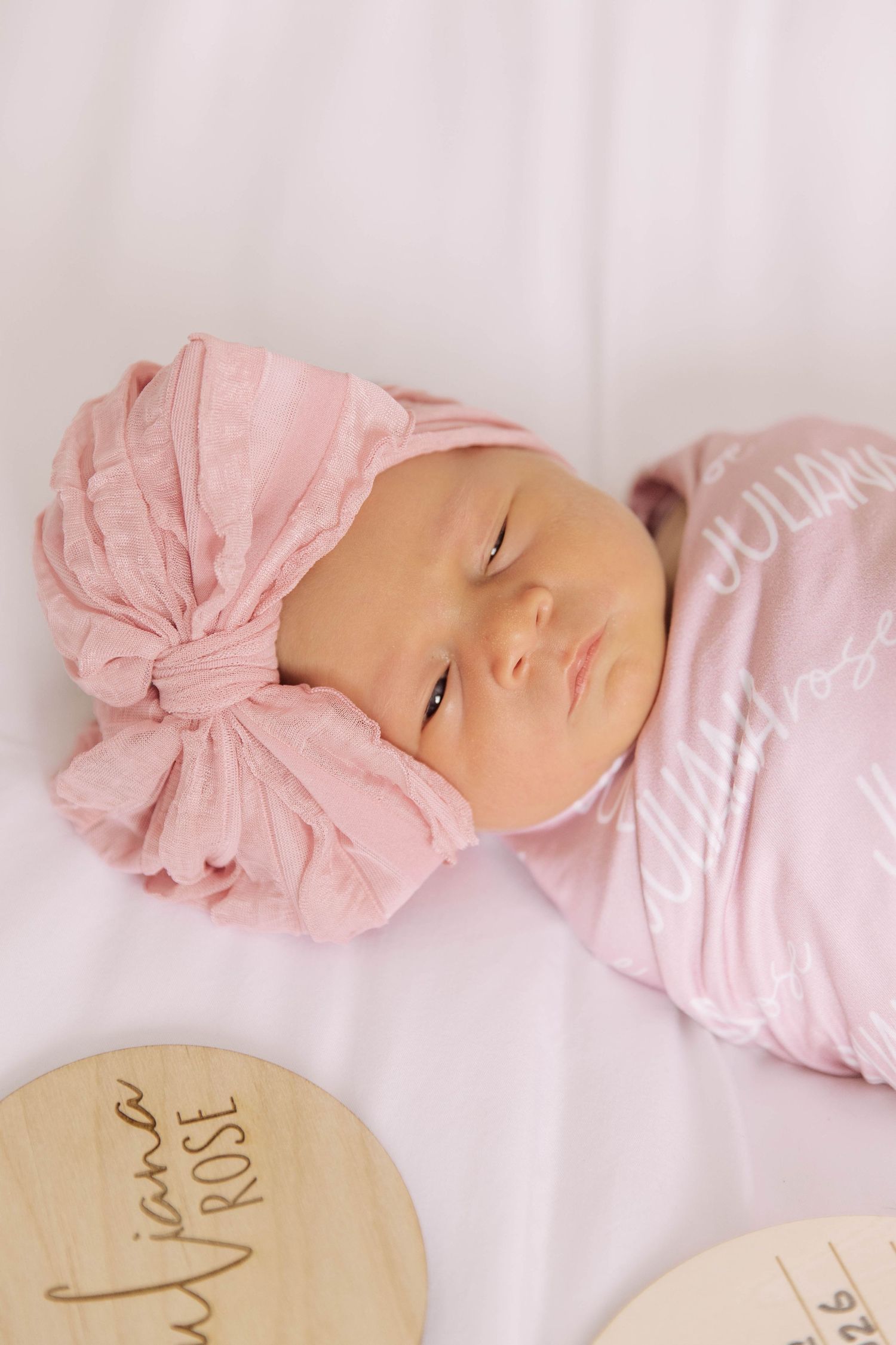 Newborn baby girl in pink turban wrap and swaddle blanket with name Juliana Rose displayed.