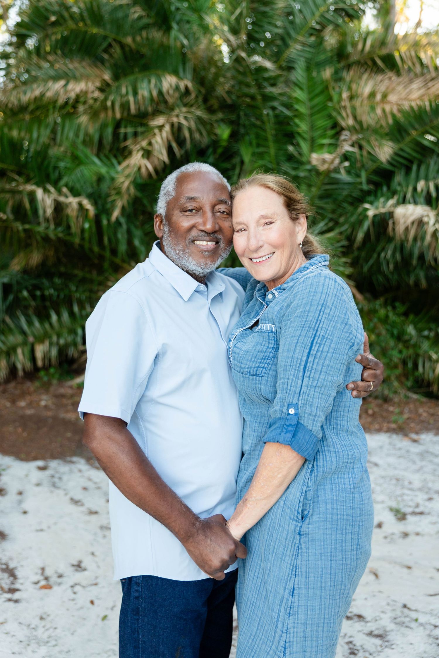 A smiling older interracial couple embraces warmly in front of lush tropical greenery in Wesley Chapel.