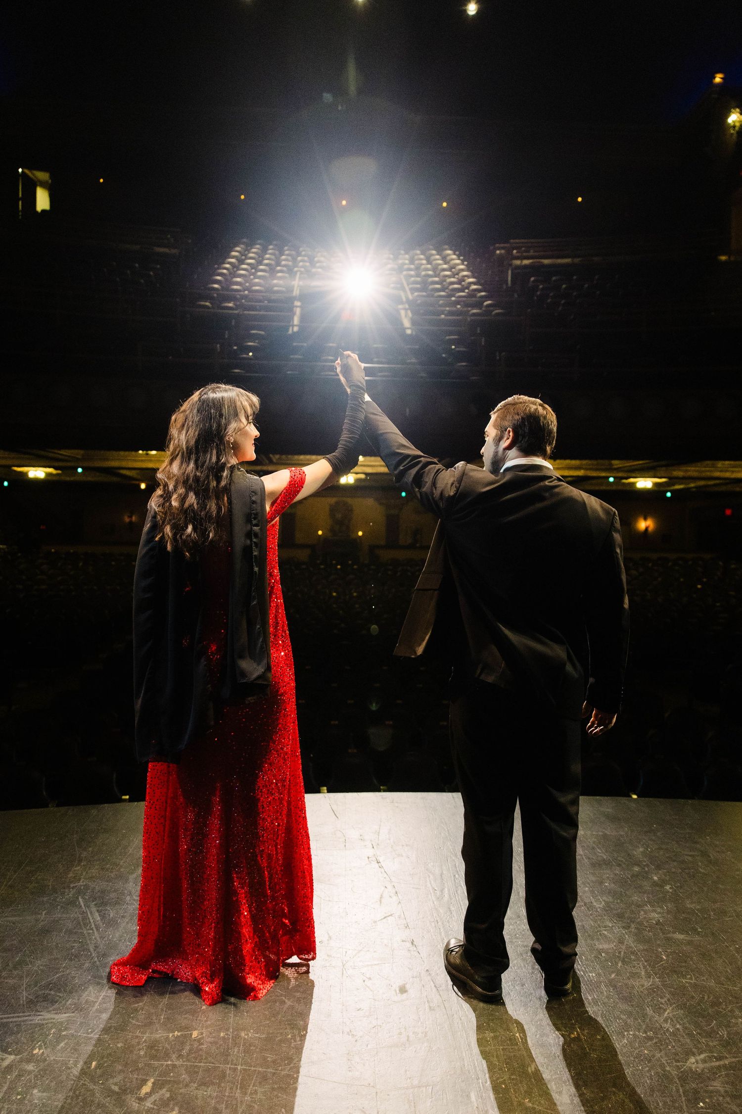 Couple in formal wear holding hands raised on stage under a bright spotlight at the Tampa Theatre.